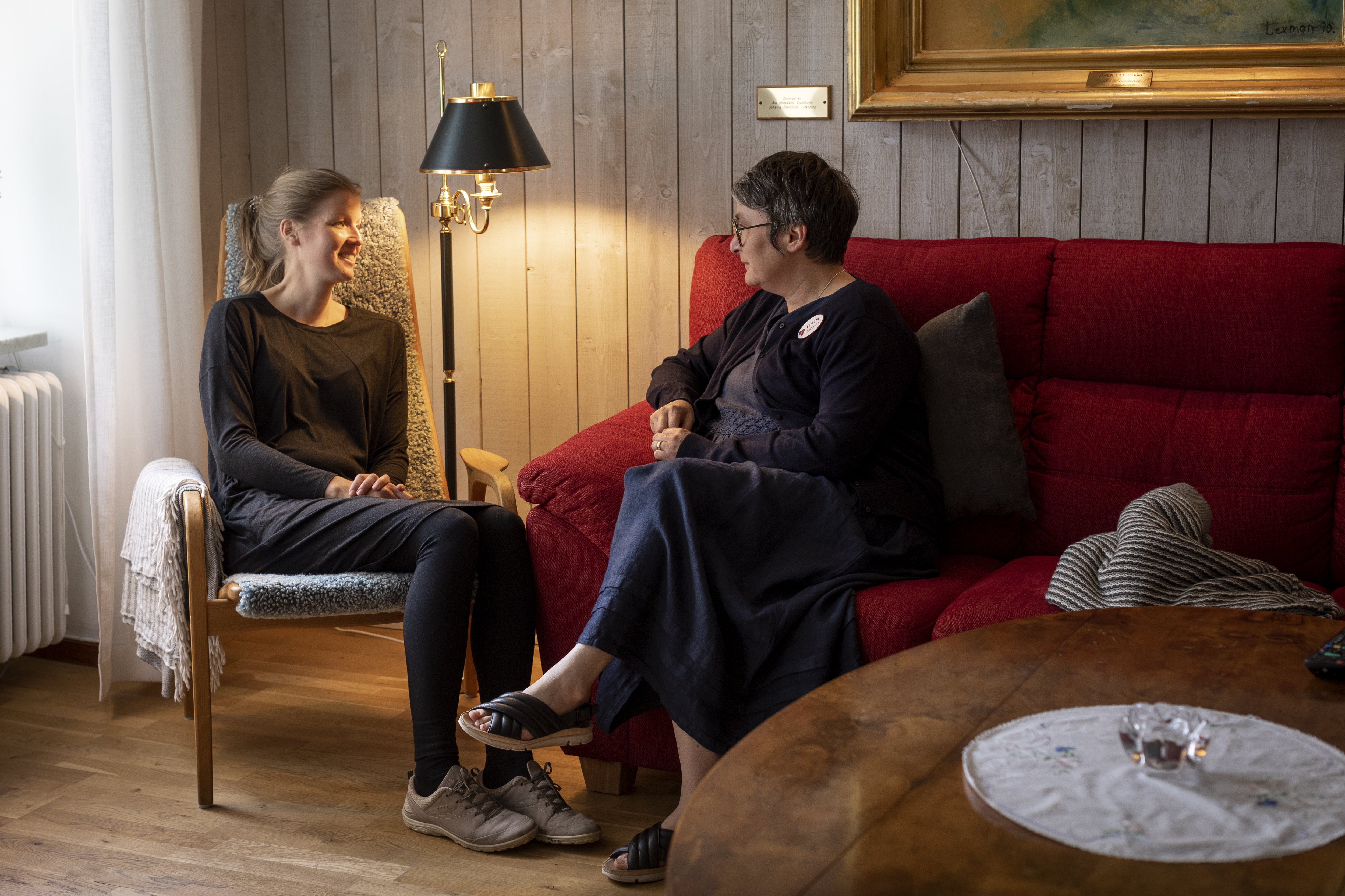 Två kvinnor sitter och samtalar i ett vardagsrum.