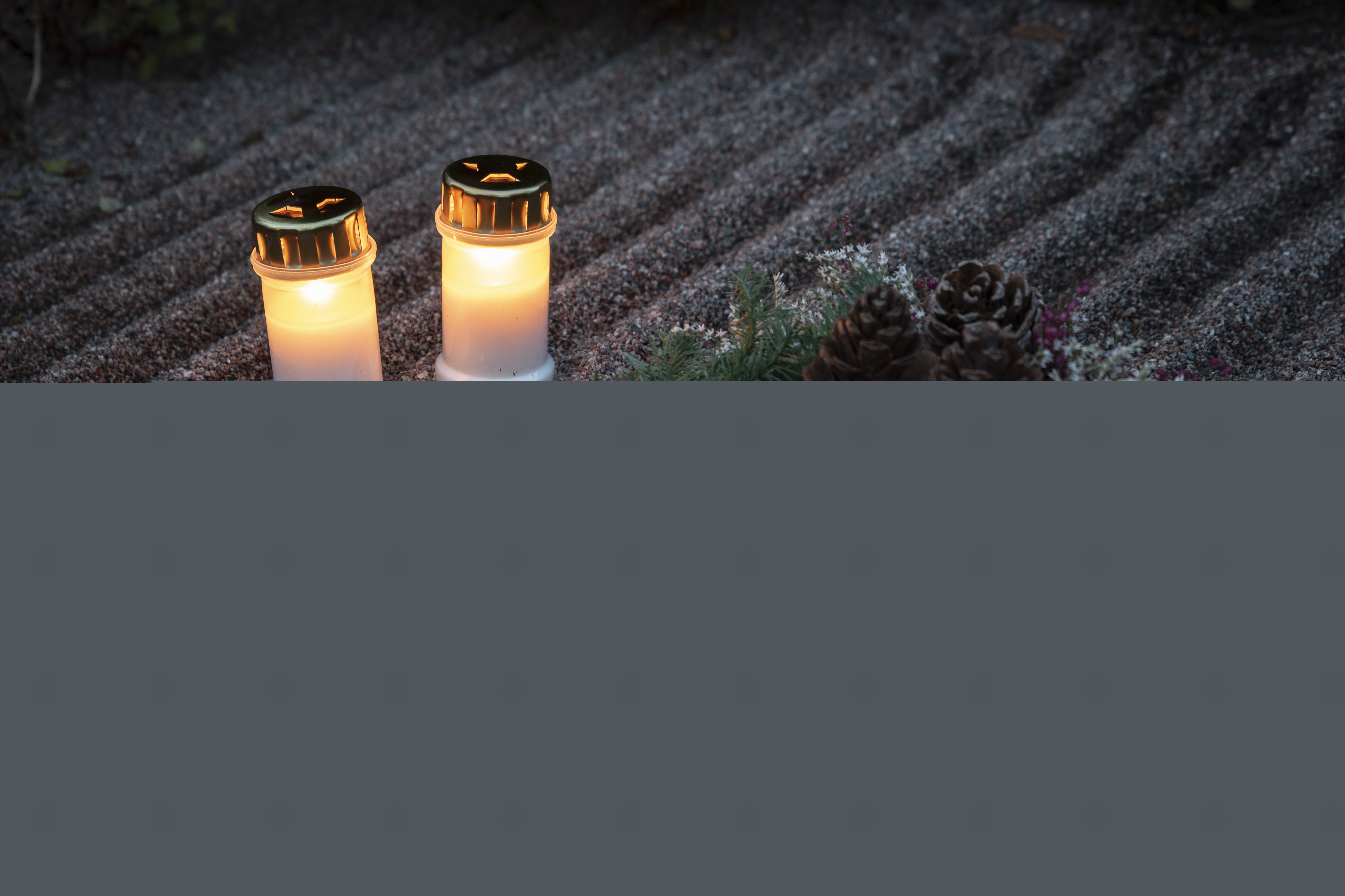 Två tända gravljus och en grankrans på en grav.