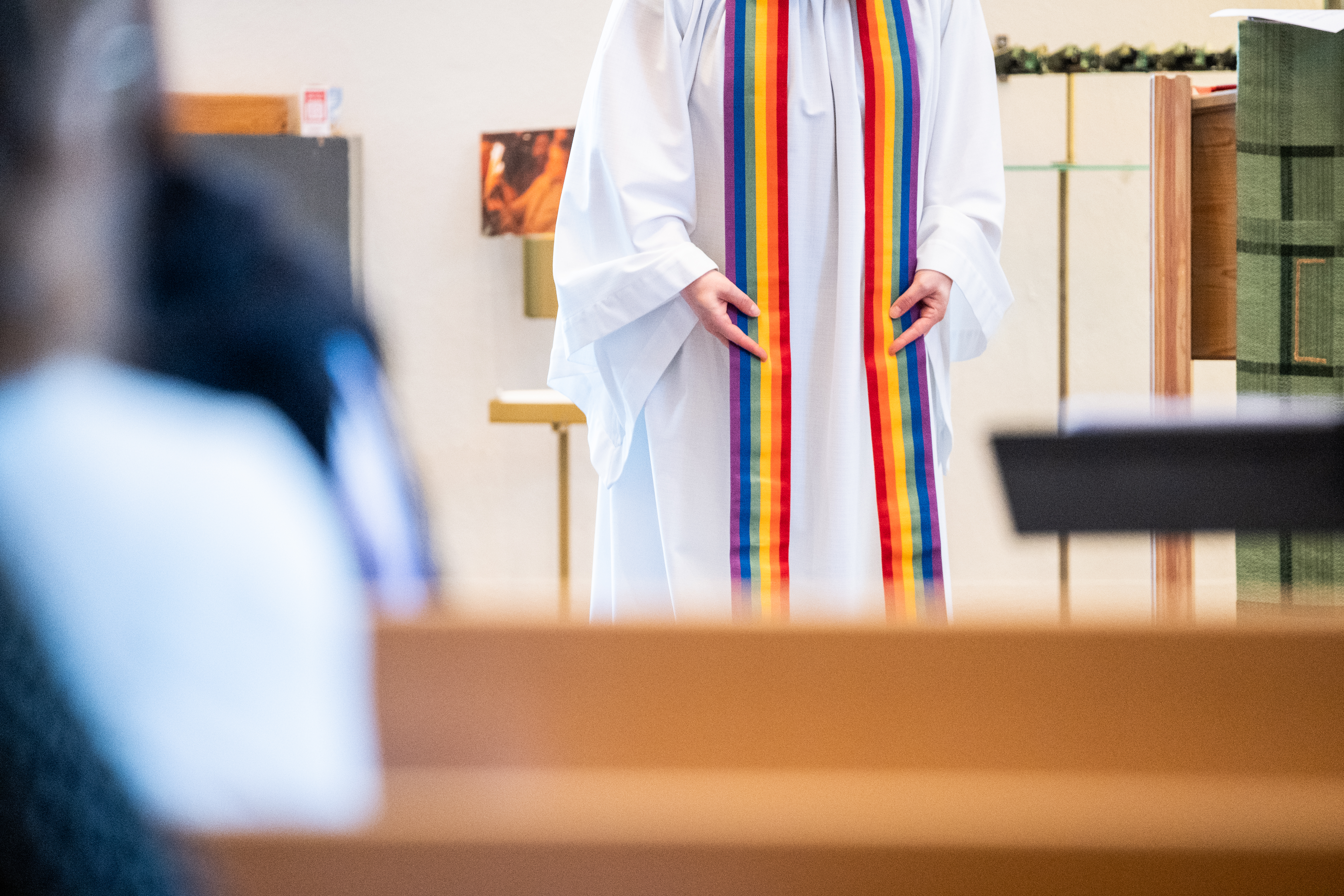 En präst har en regnbågsfärgad stola över axlarna.