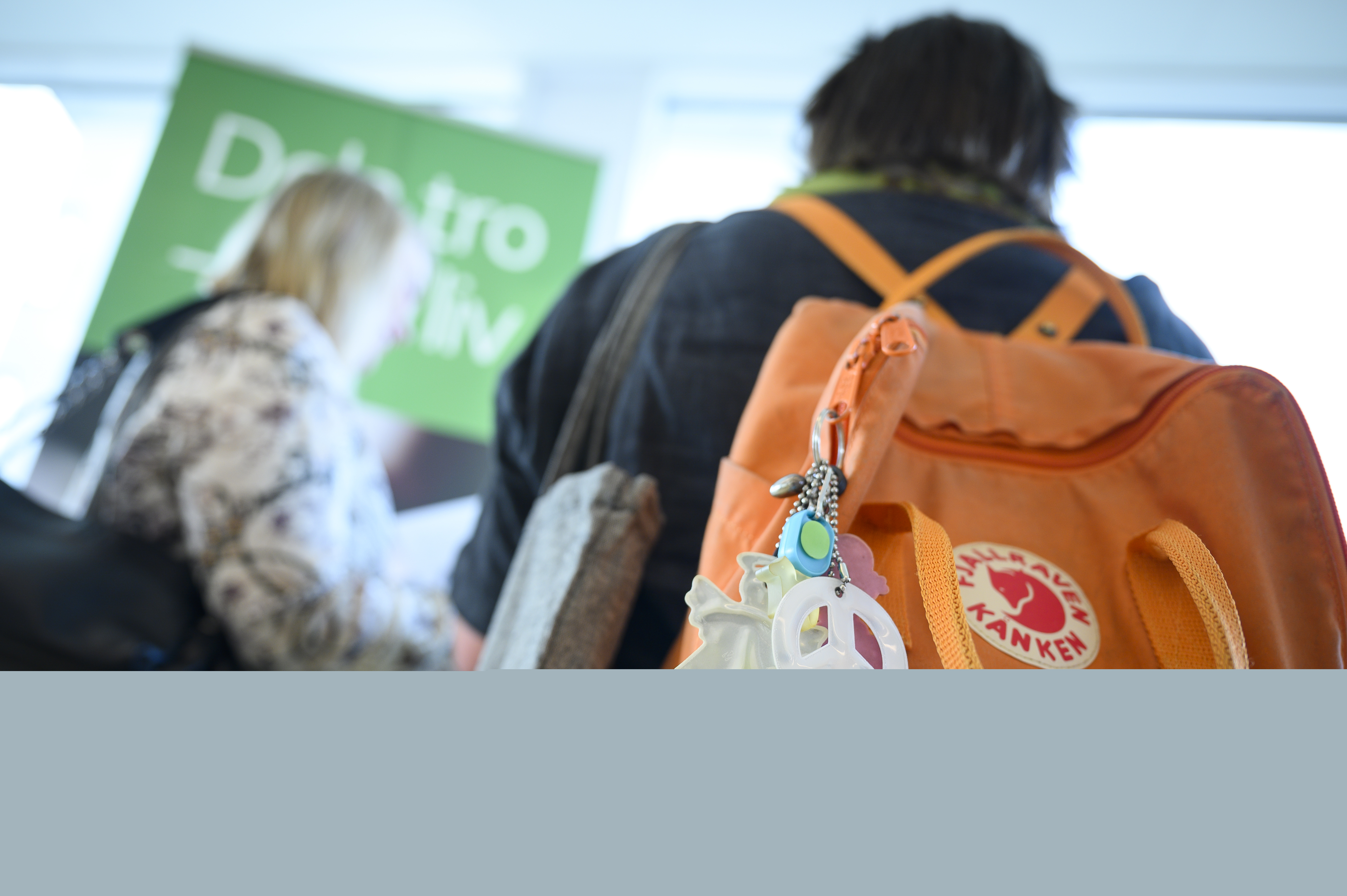 Två personer på konferens eller mässa. Personen närmast kameran har en ryggsäck med olika reflexer hängande.