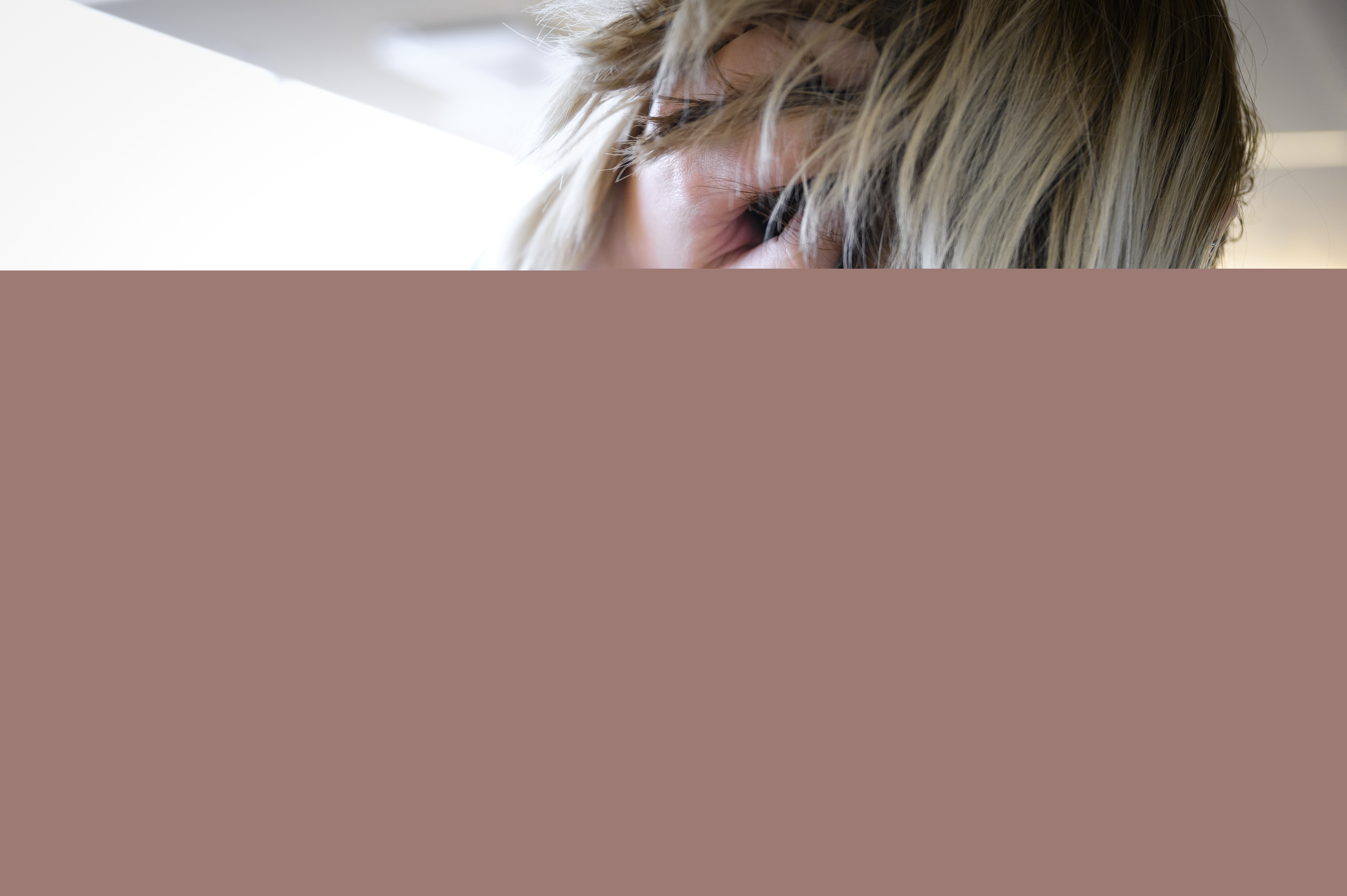 En kvinna lyfter upp sitt blonda hår i nacken för att visa en tatuering som föreställer ett kors.