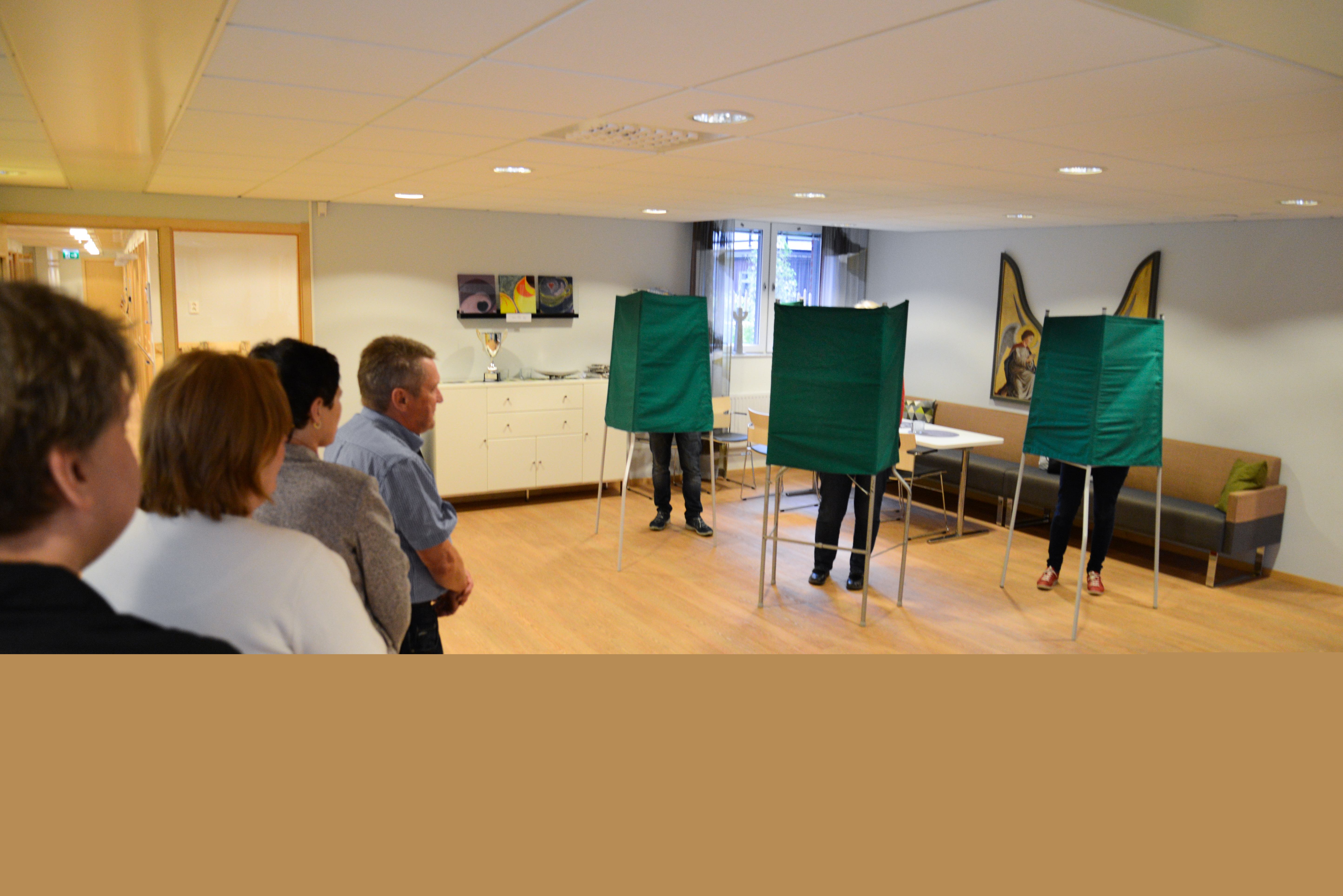 Några personer står i kö i en vallokal.