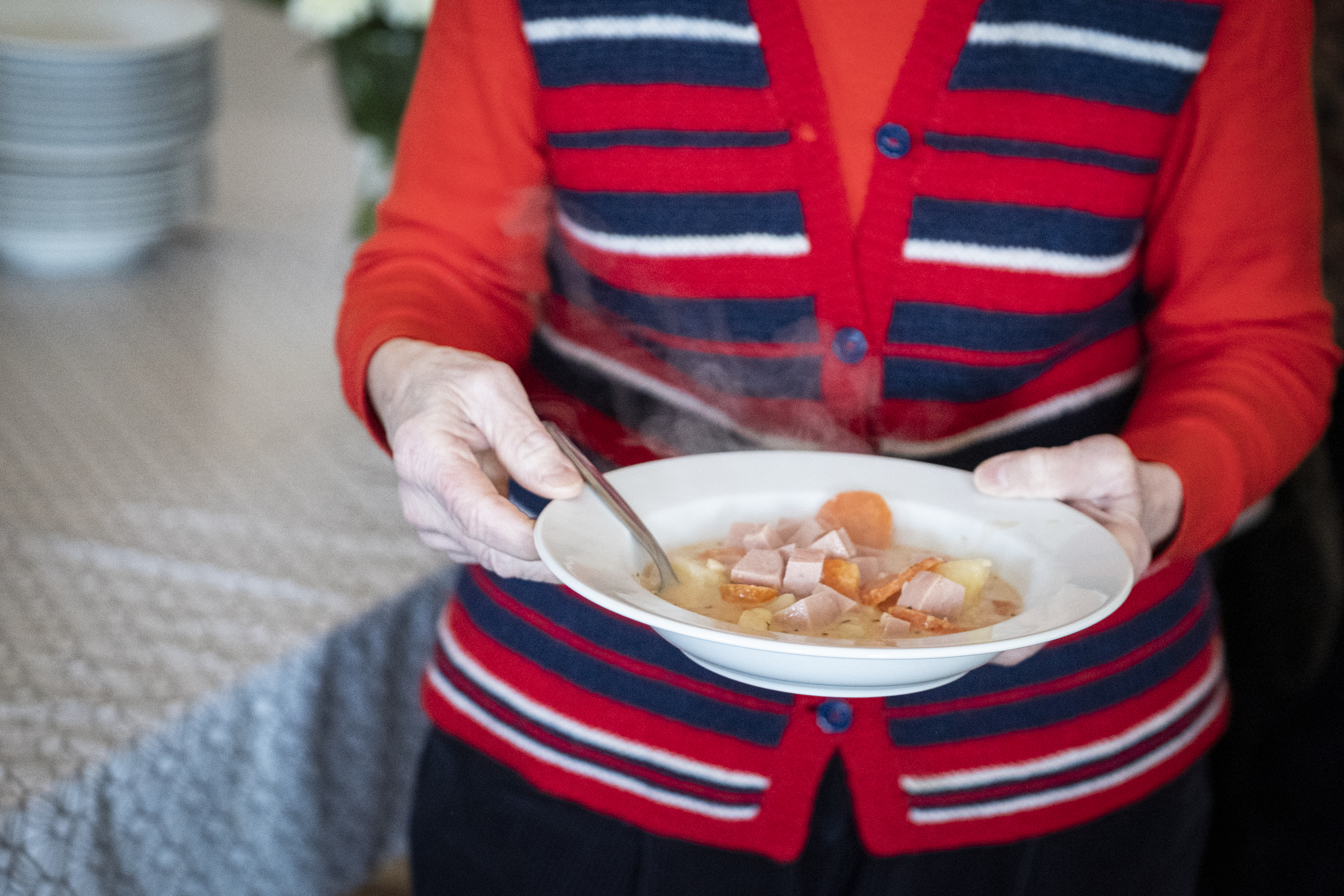 En äldre kvinna bär på en rykande het sopptallrik.