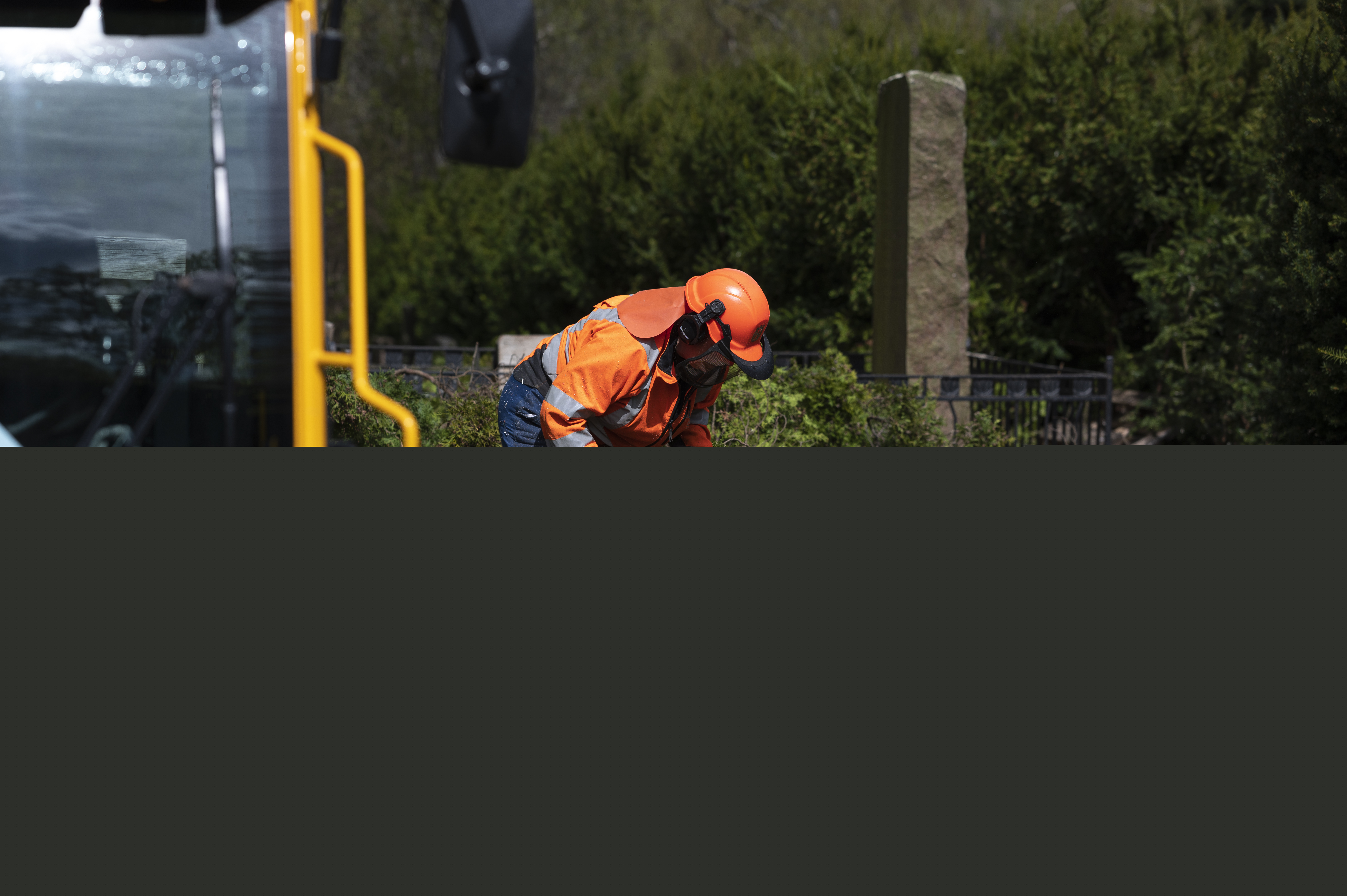En kyrkogårdsarbetare sågar av ett nedhugget träd med en motorsåg.