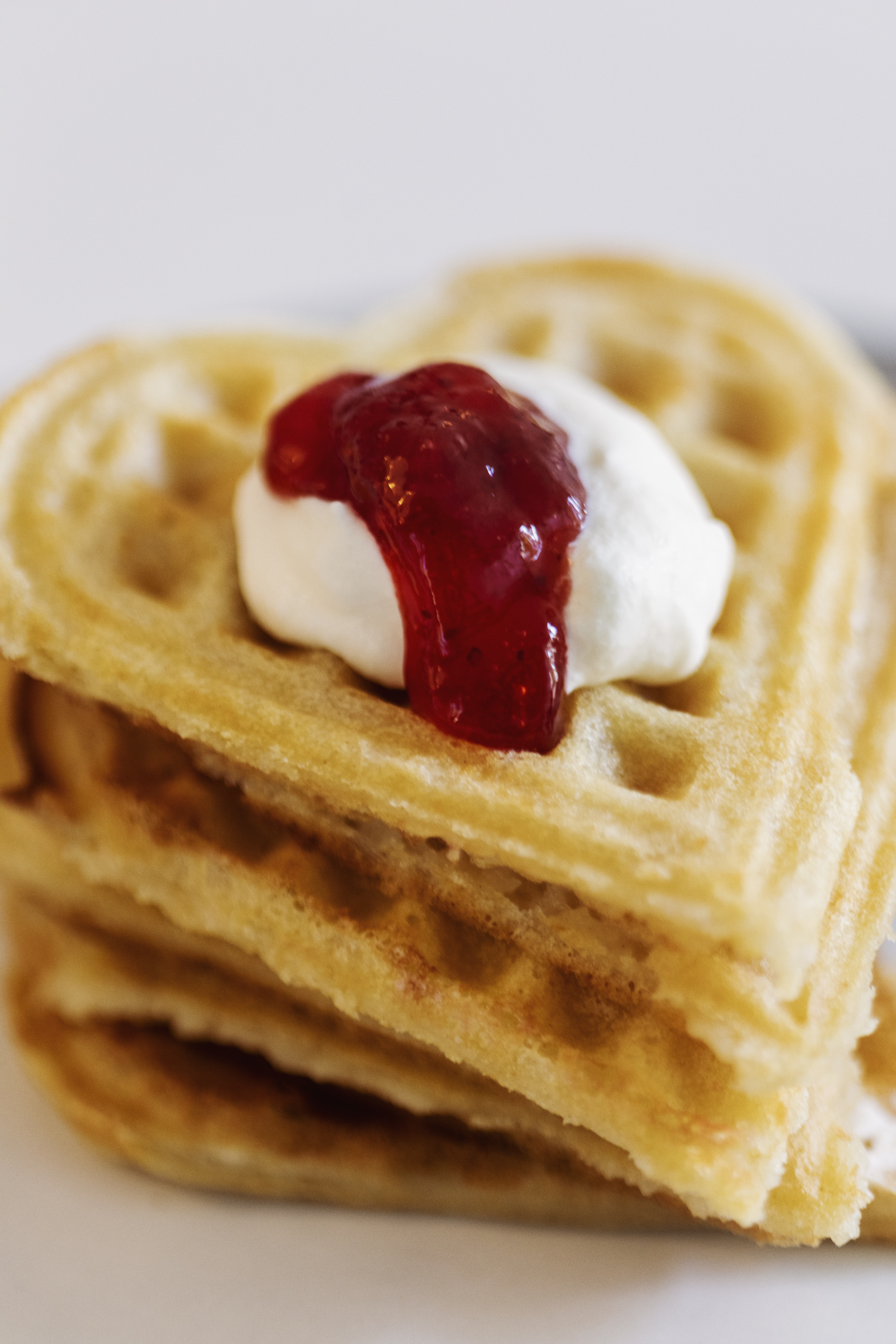 En hög med hjärtformade våfflor, med sylt och grädde på toppen.