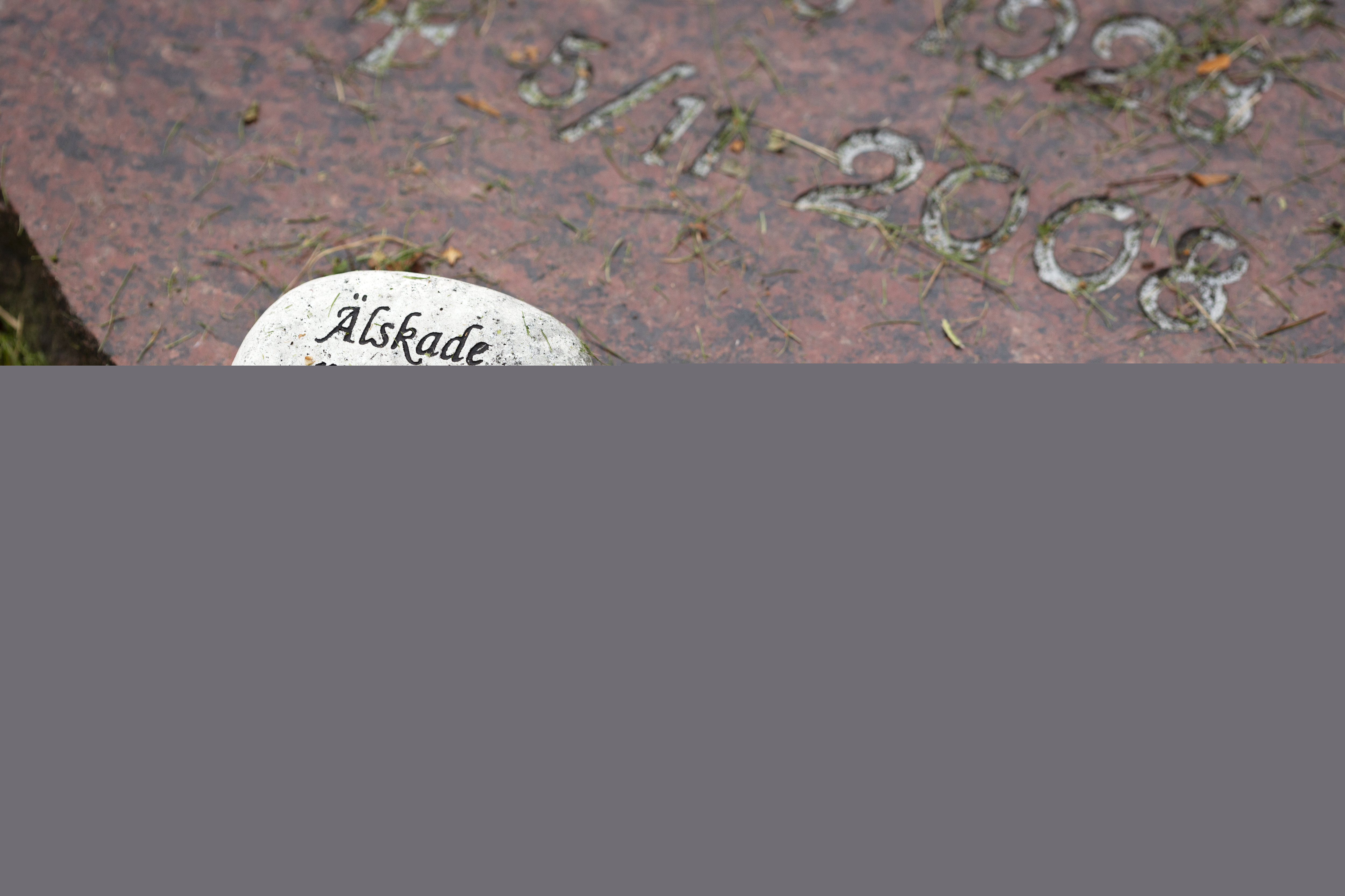 Liten sten med texten "älskade mamma" inristad ligger på en gravsten.