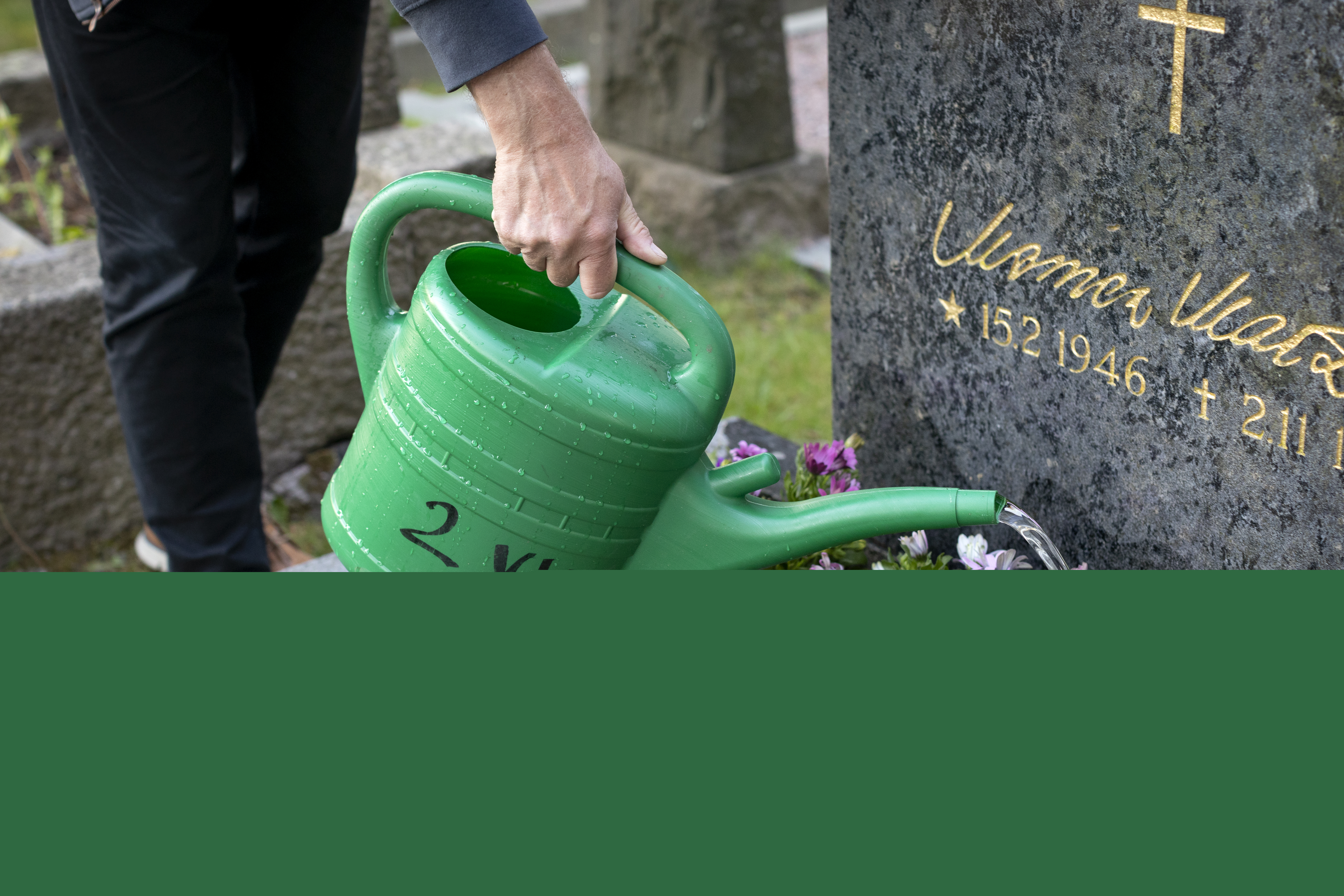 Någon vattnar blommorna på en grav.