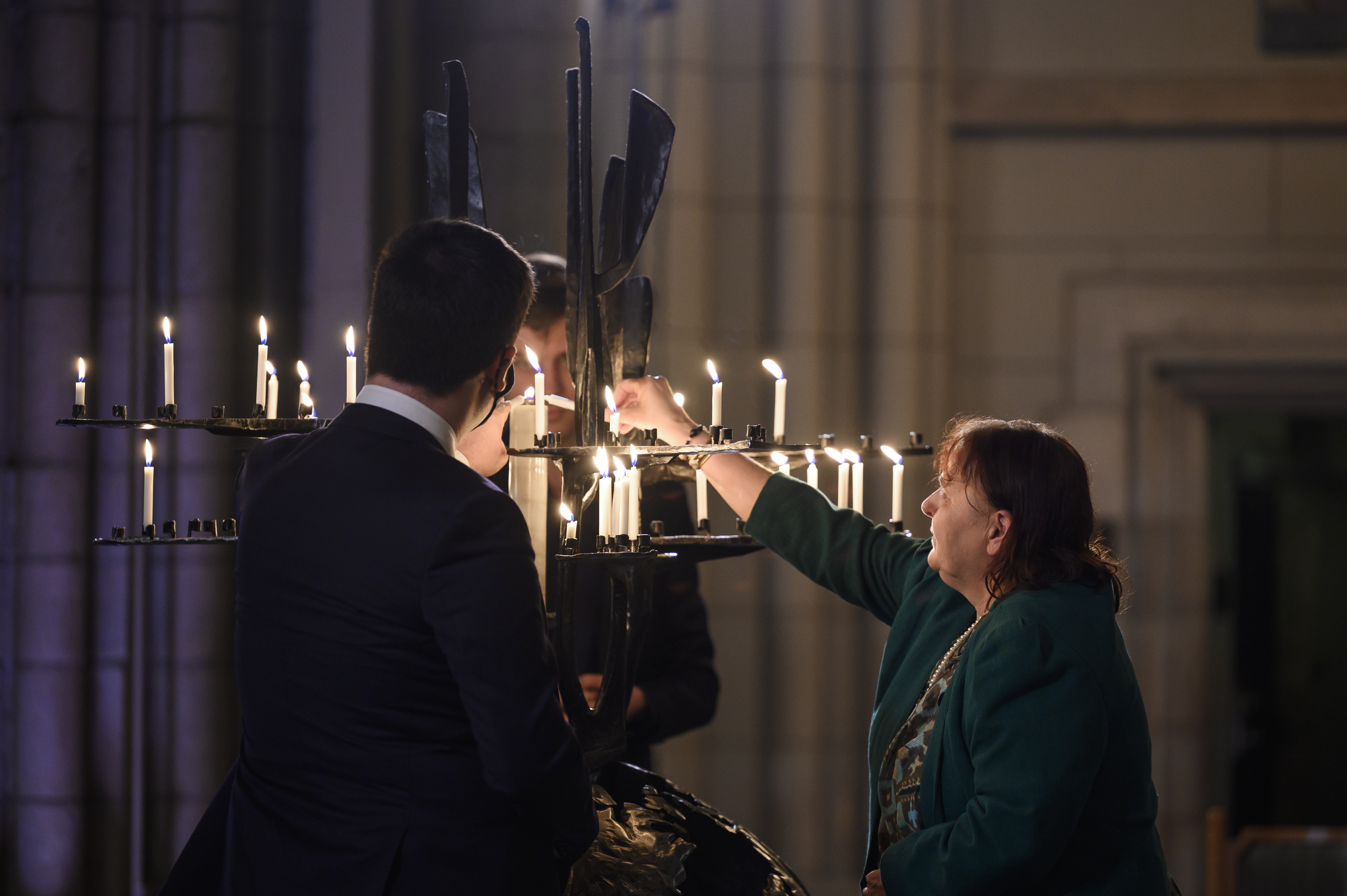 Några personer tänder ljus i järnskulpturen Folkförsoningens träd i Uppsala domkyrka.