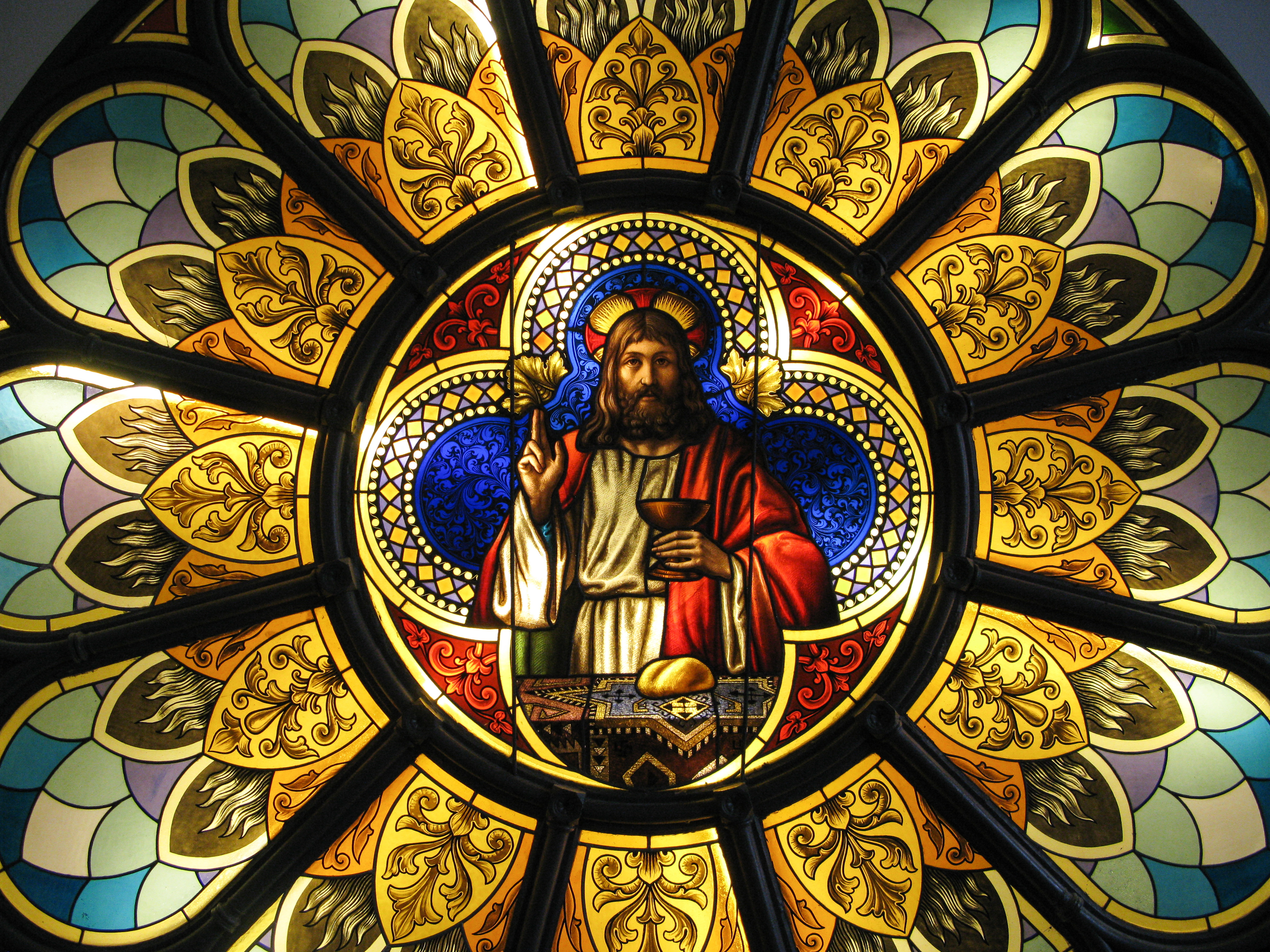 Ett runt kyrkfönster. I mitten syns Jesus som delar ut nattvard.