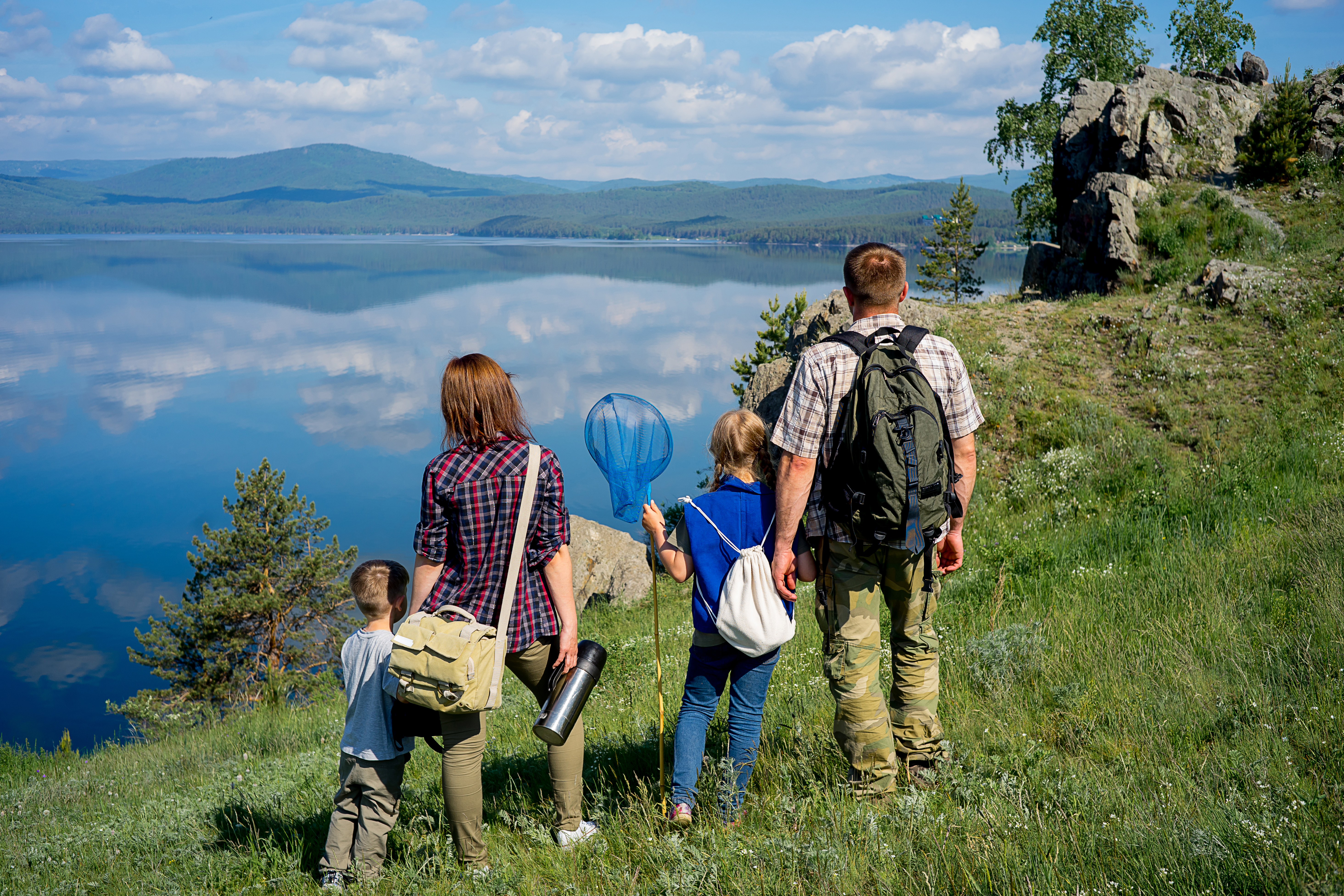 En familj med två barn står och tittar ut över en spegelblank sjö med fjäll i bakgrunden.