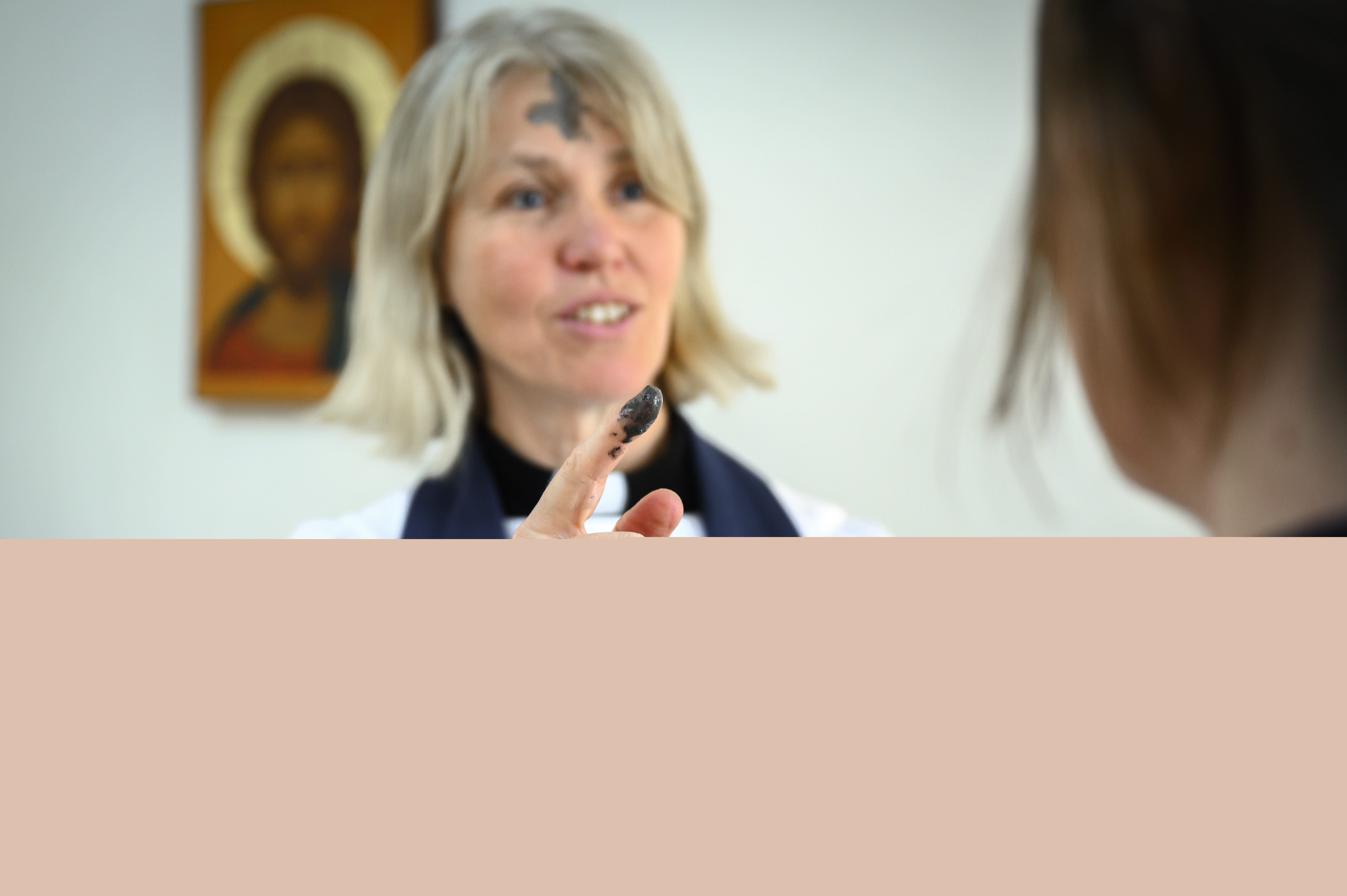 Kvinnlig präst med askkors i pannan har doppat fingret i askan för att göra ett likadant kors på personen framför henne.