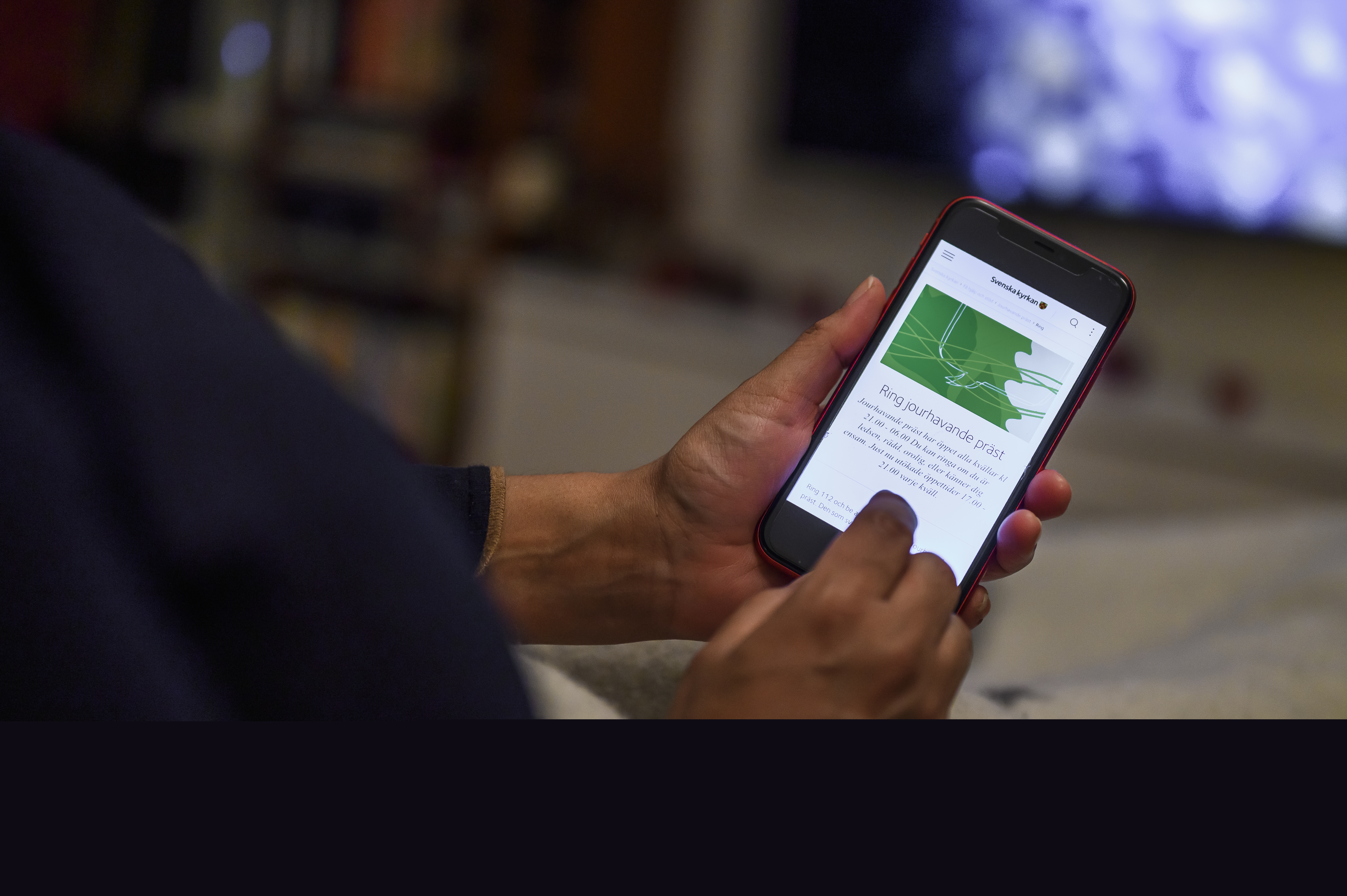 En person har sin mobiltelefon i händerna. Skärmen visar Svenska kyrkans information om jourhavande präster.