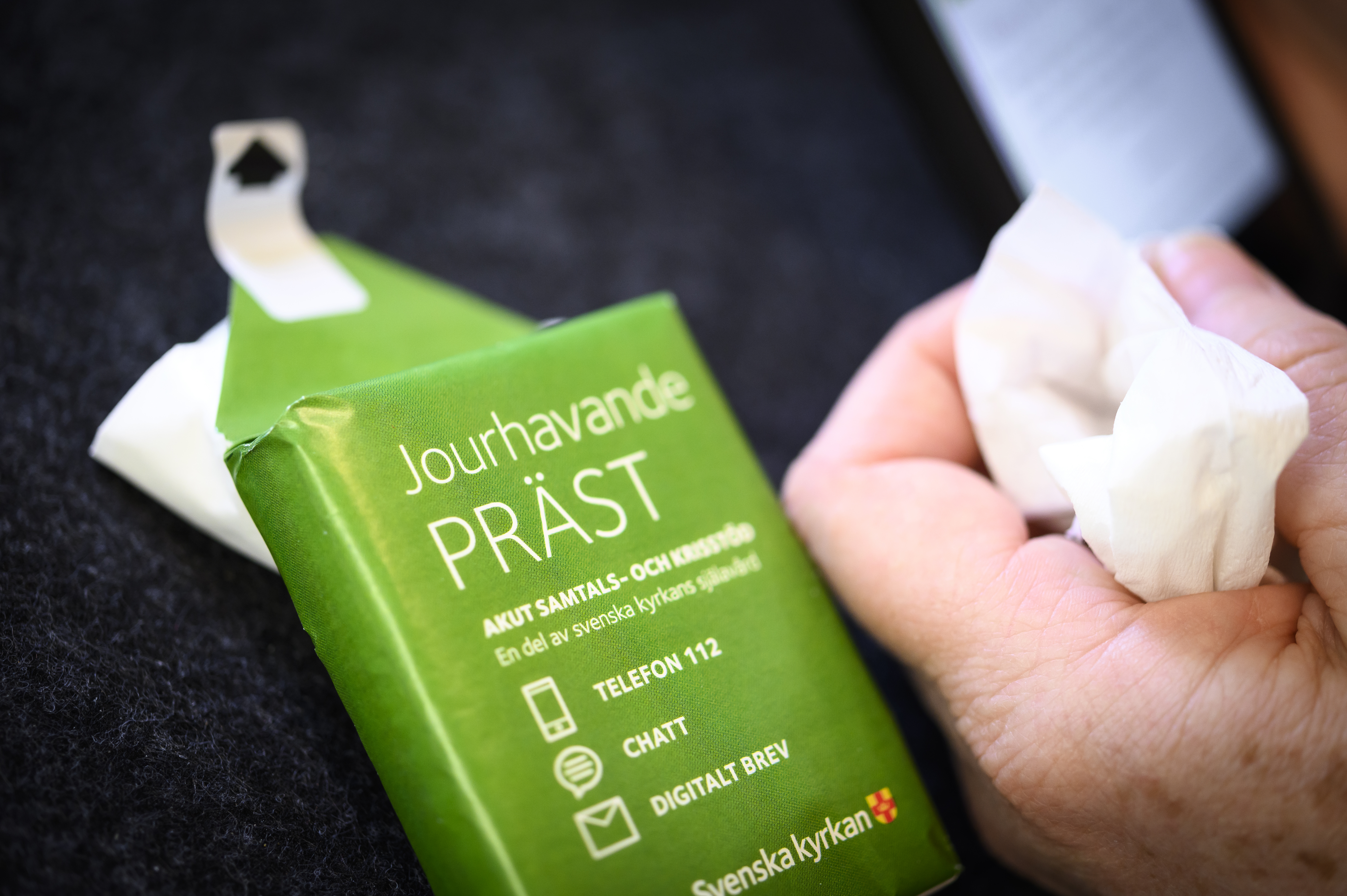 Någon håller en näsduk i handen. En förpackning med visitkort till jourhavande präst ligger bredvid.