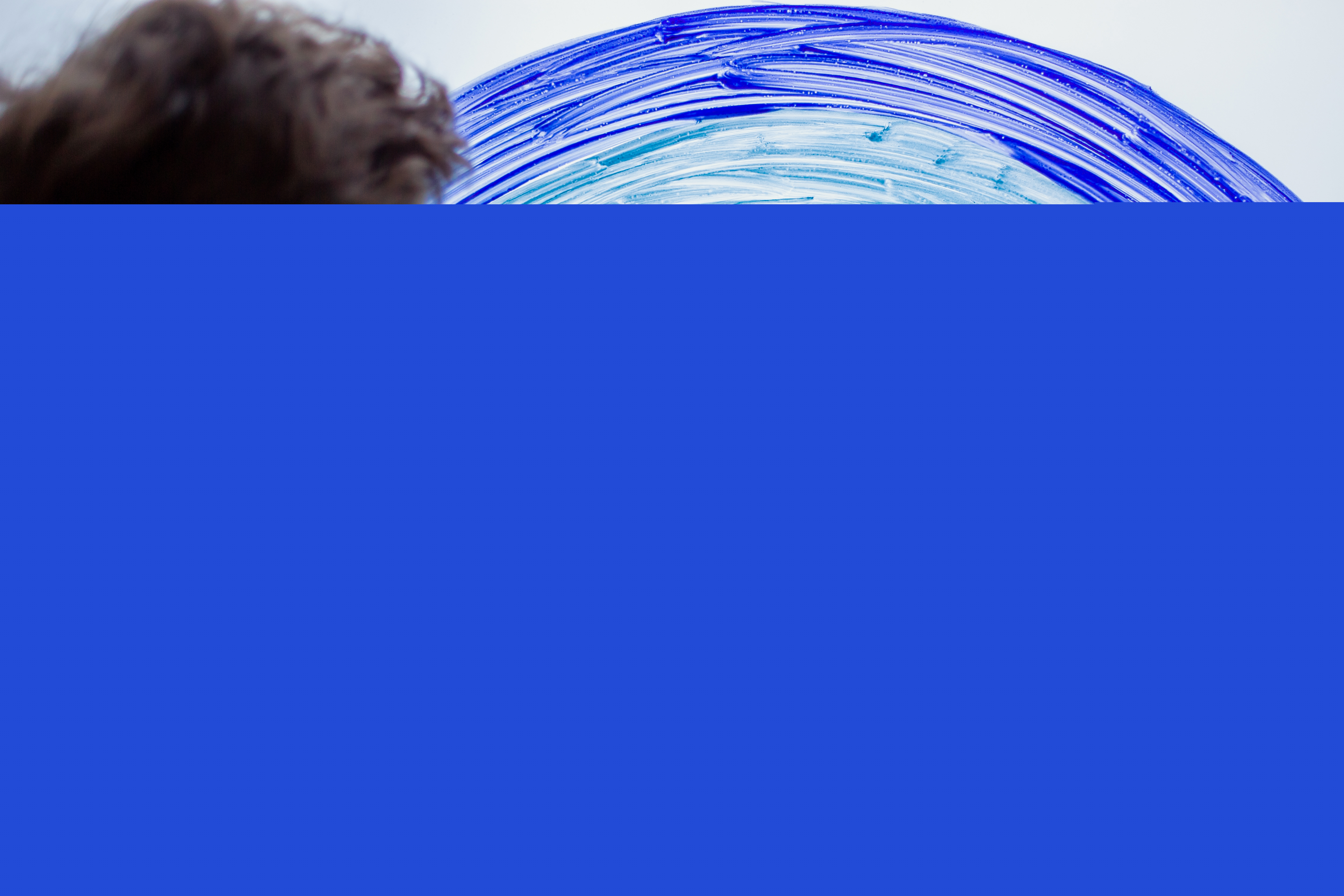 En liten pojke håller handen på en regnbåge målad på ett fönster.