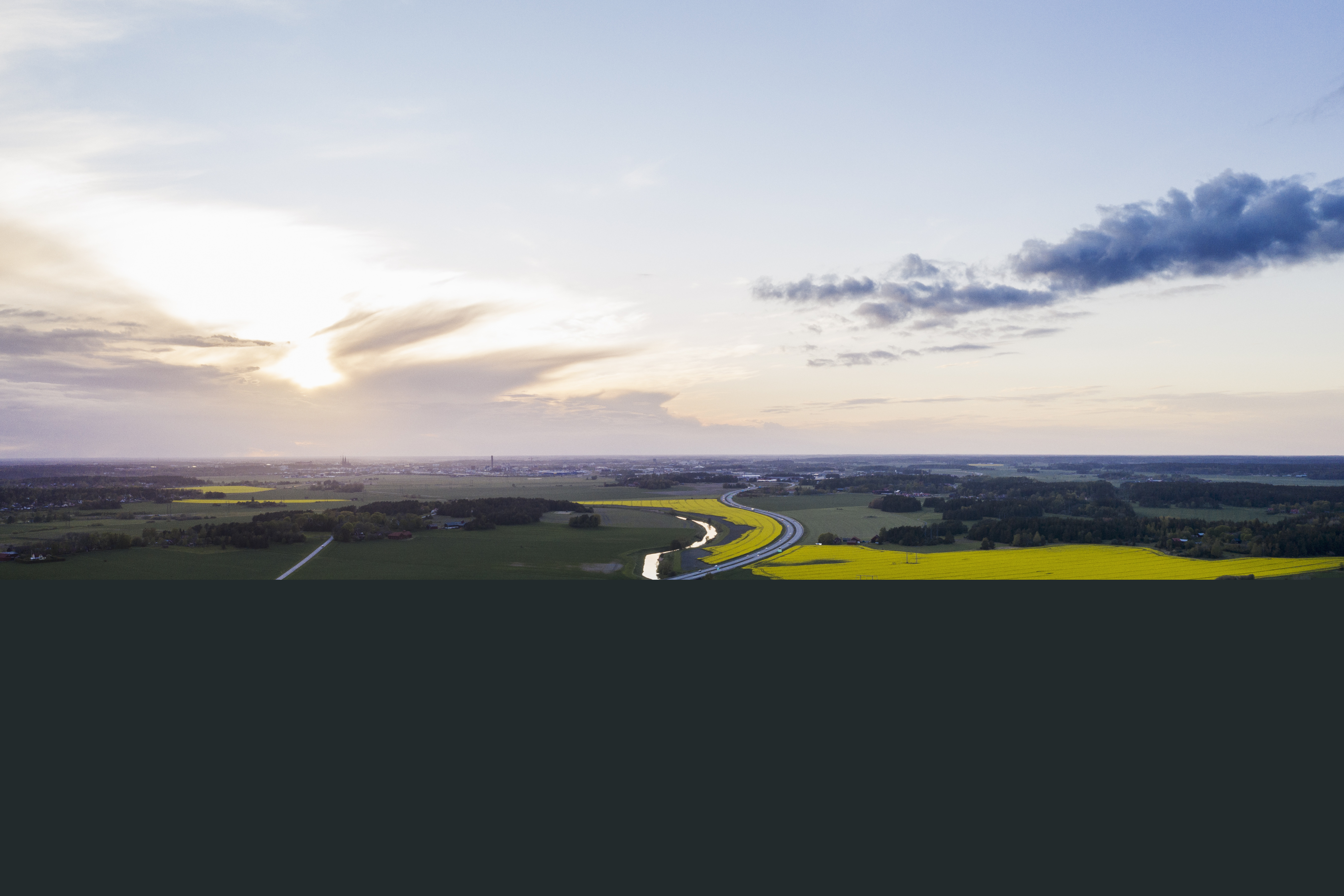 Flygfoto över en bilväg och en å genom ett fält.