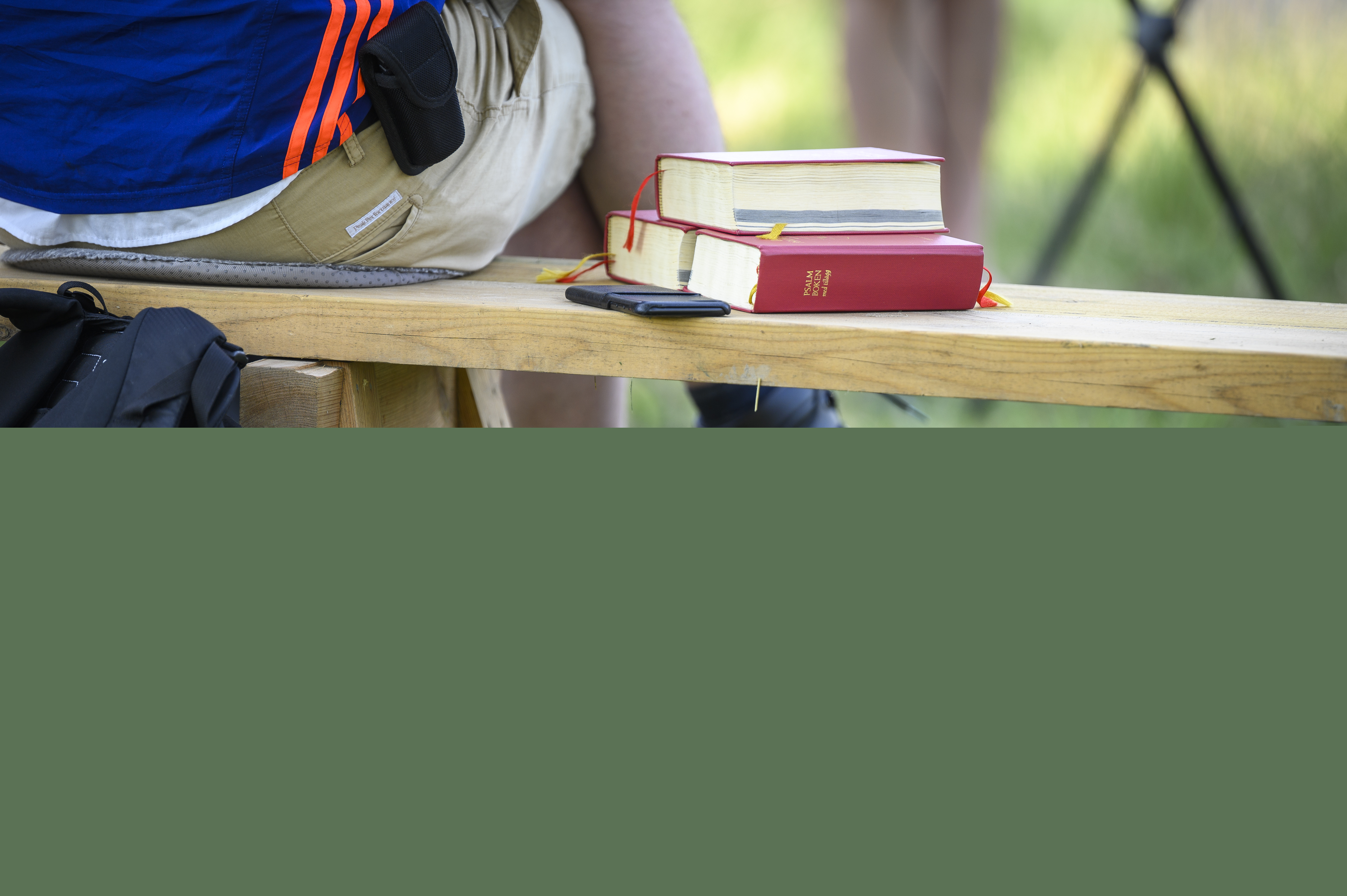 Någon sitter på en bänk utomhus. Bredvid ligger några psalmböcker.