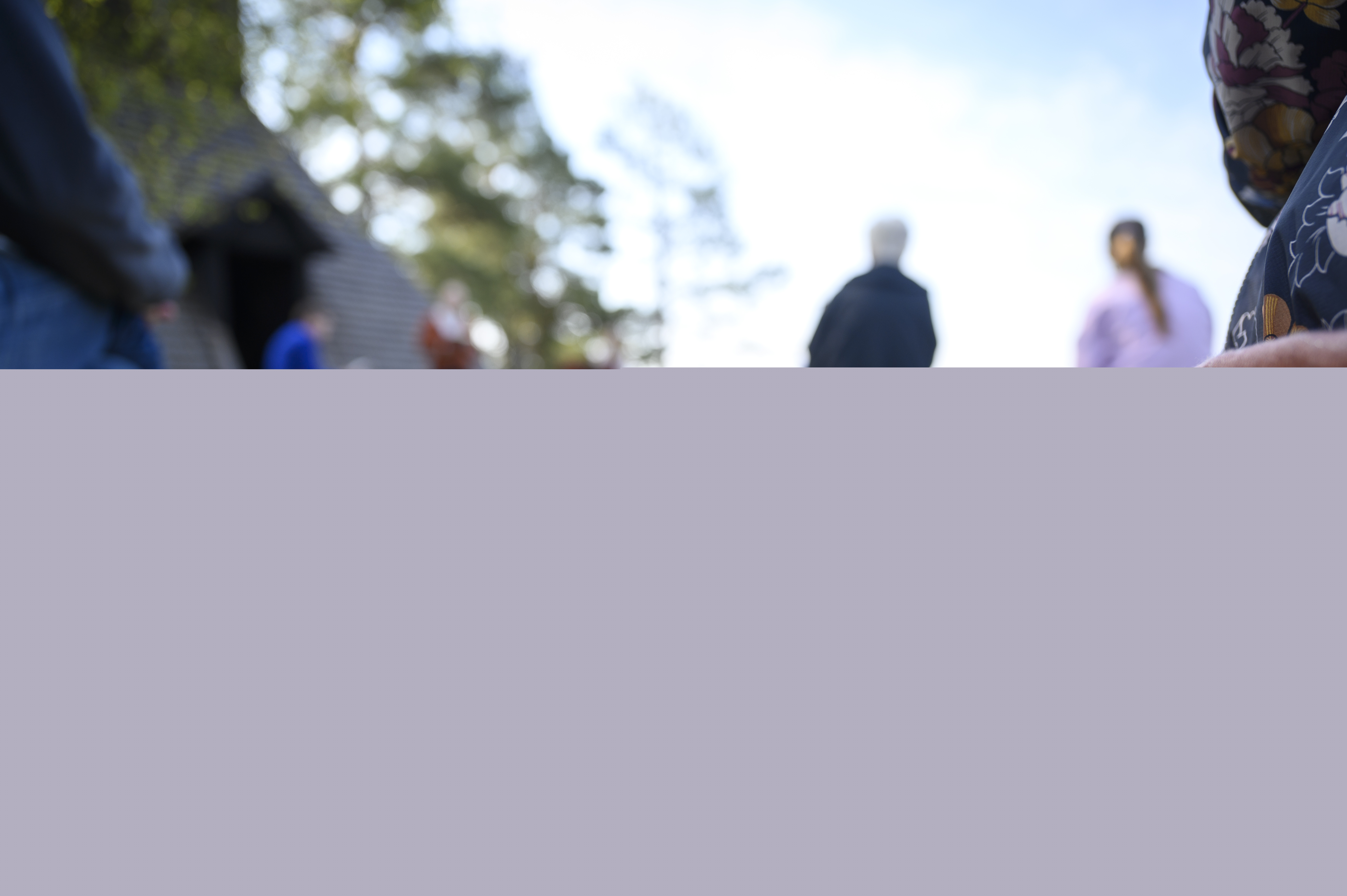 Ett par solglasögon och några psalmböcker ligger på en bänk utomhus. Människor syns i bakgrunden.