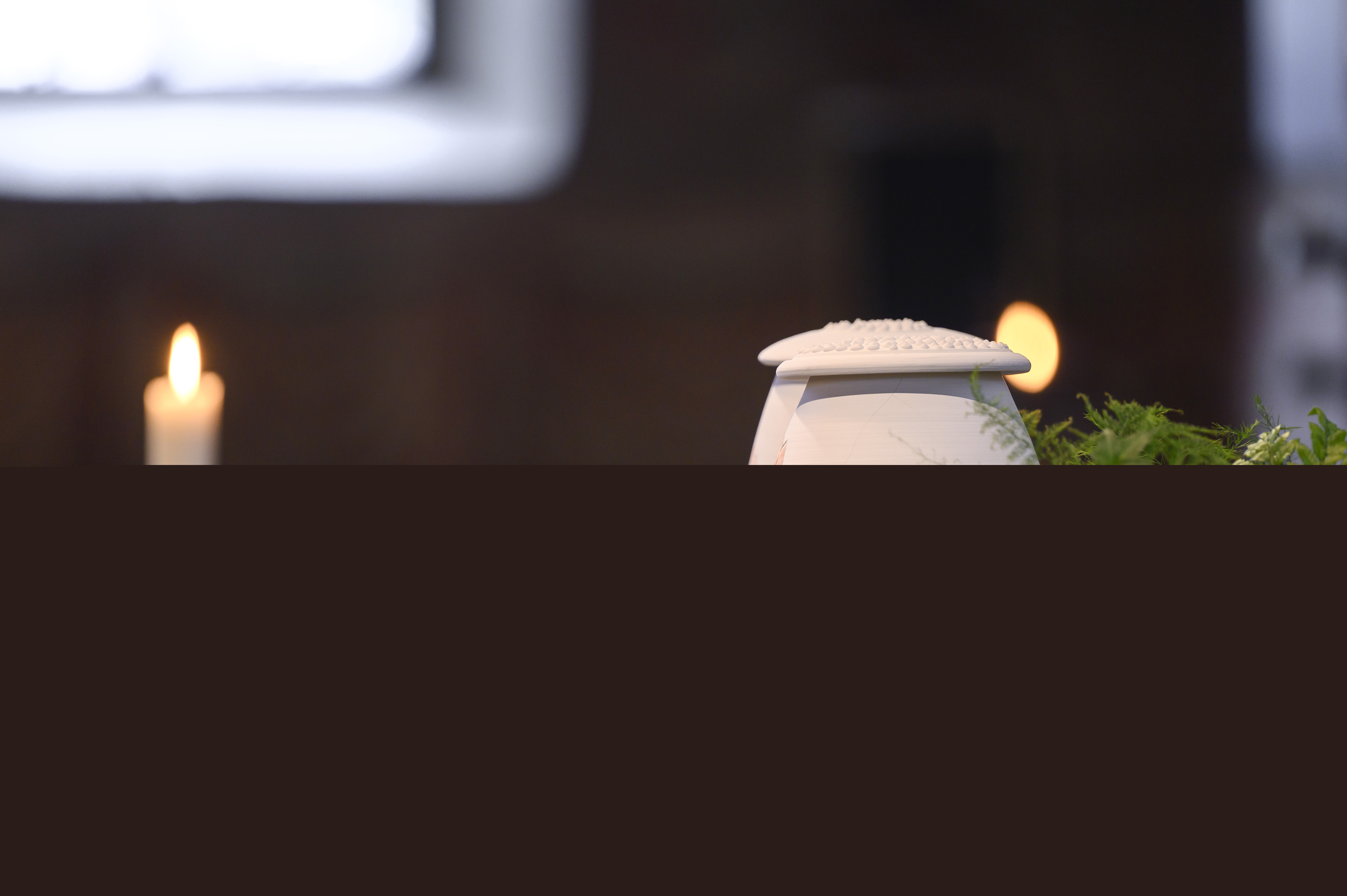 Två urnor står bland ormbunksblad på ett bord i kyrkan.