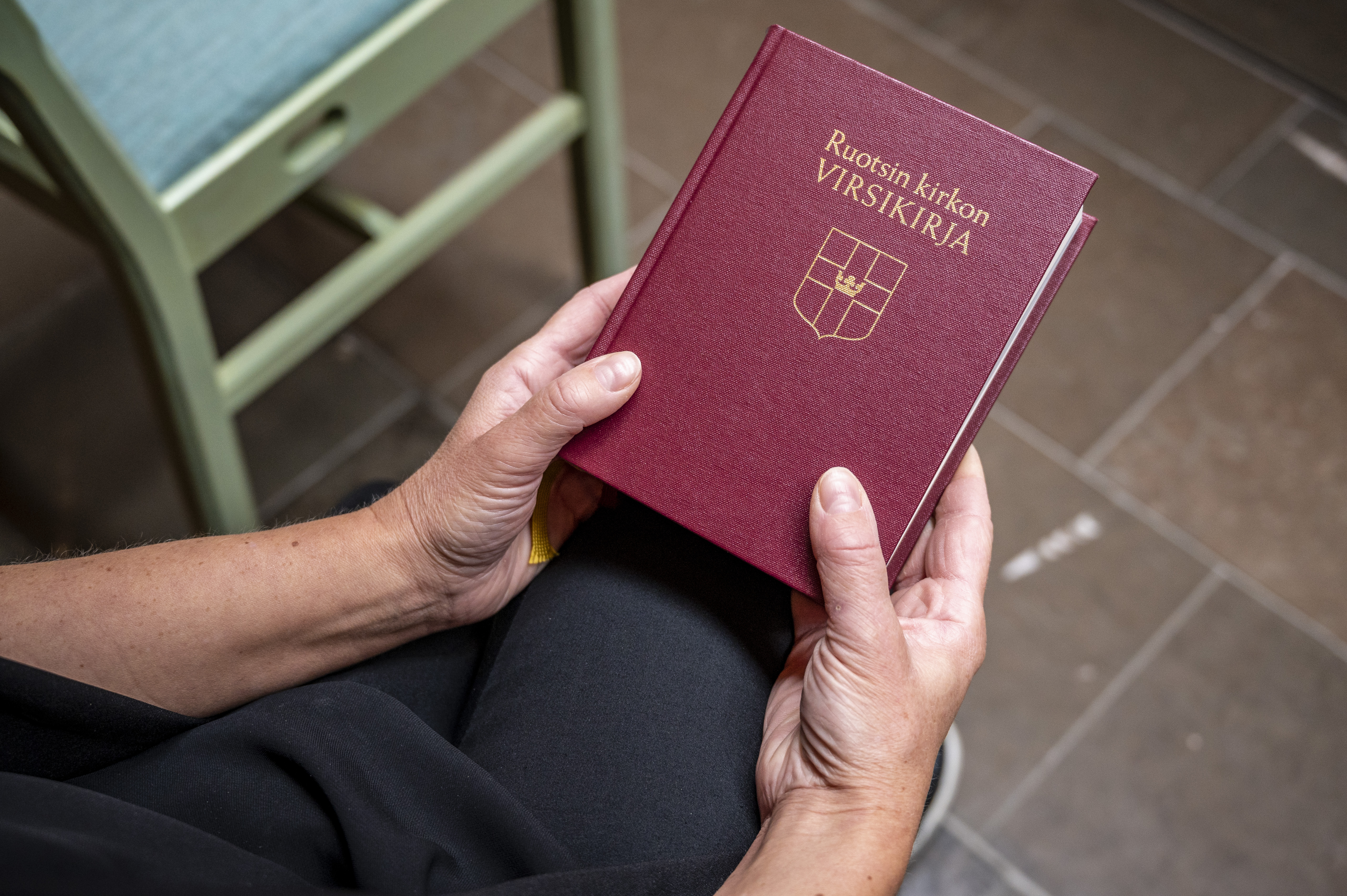 Någon sitter i ett kapell och håller en finsk psalmbok i händerna.