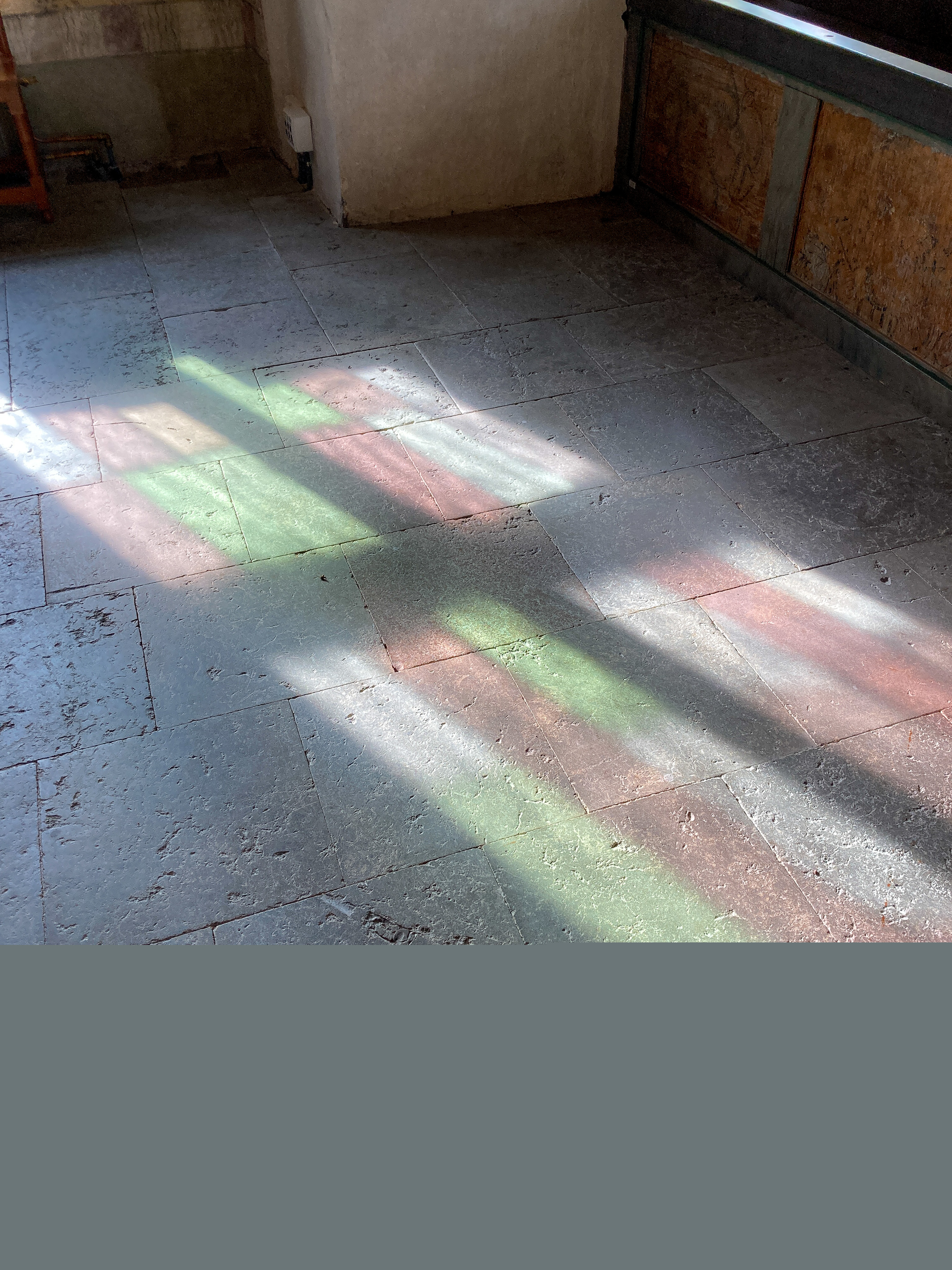 Ljuset från ett färggrant kyrkfönster reflekteras mot stengolvet i en kyrka.