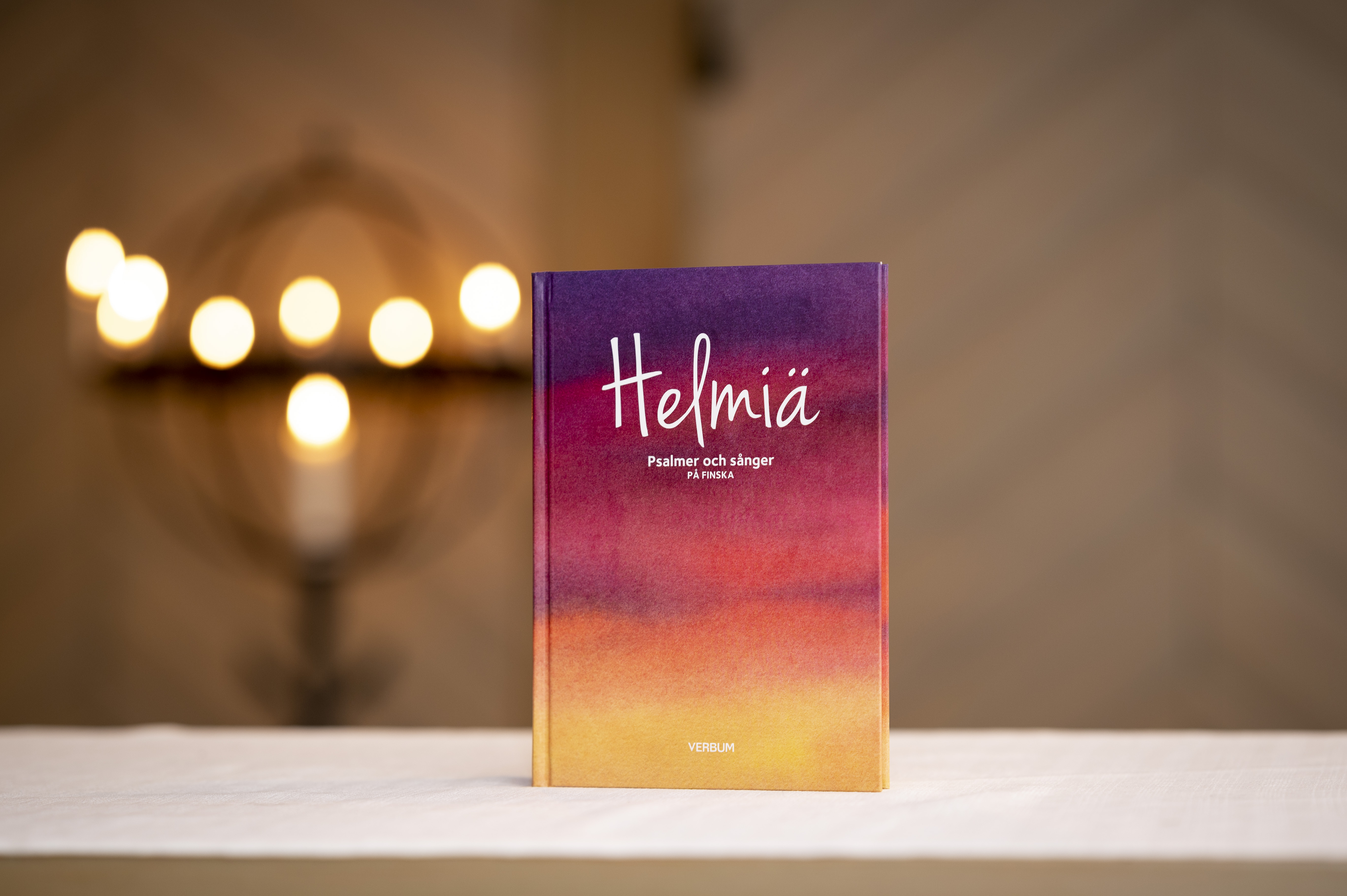En färgglad bok med psalmer och sånger på finska står uppställd på ett bord i en kyrka.