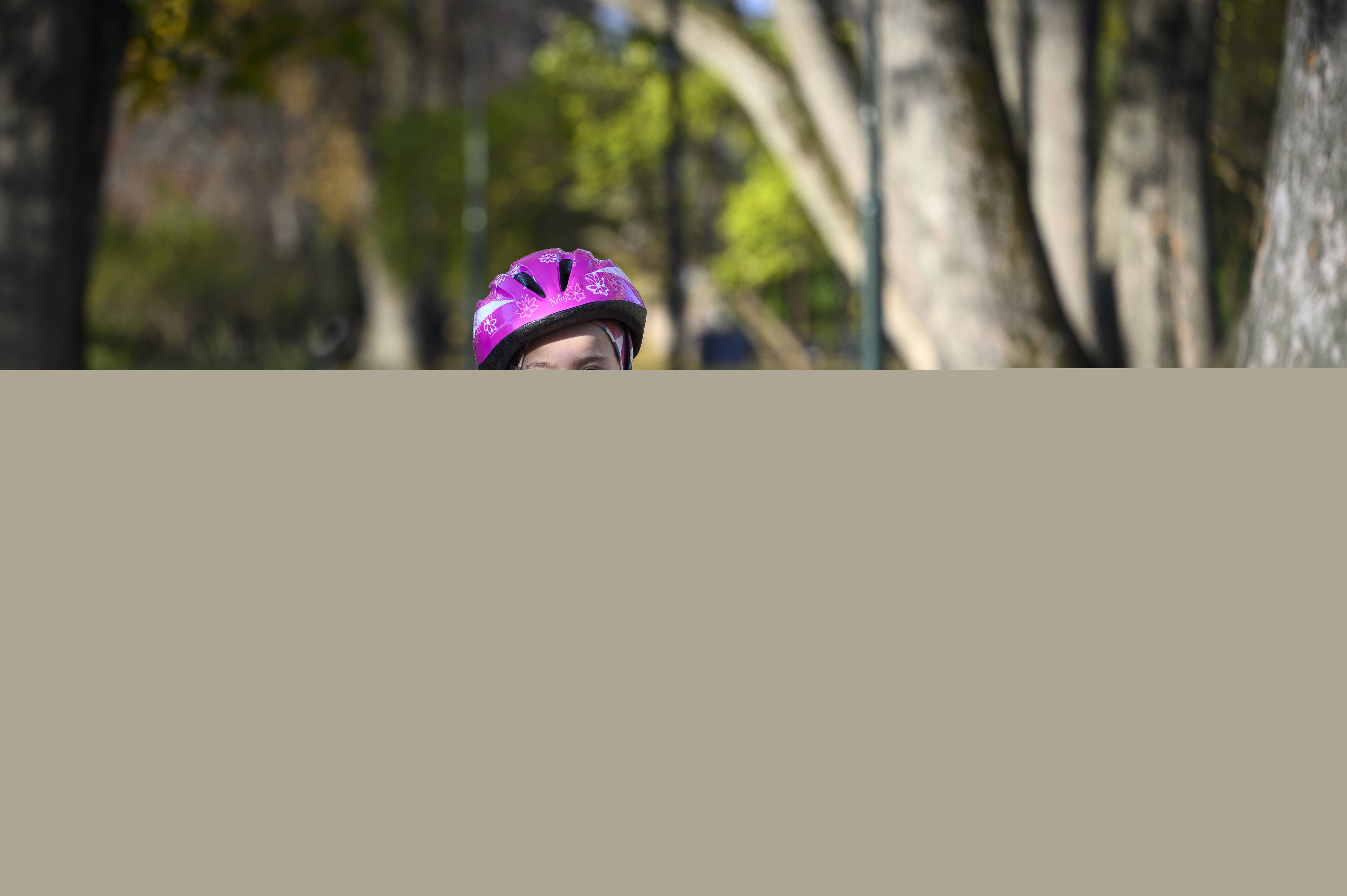 Ett barn med rosa hjälm cyklar genom en park full av höstlöv på marken.