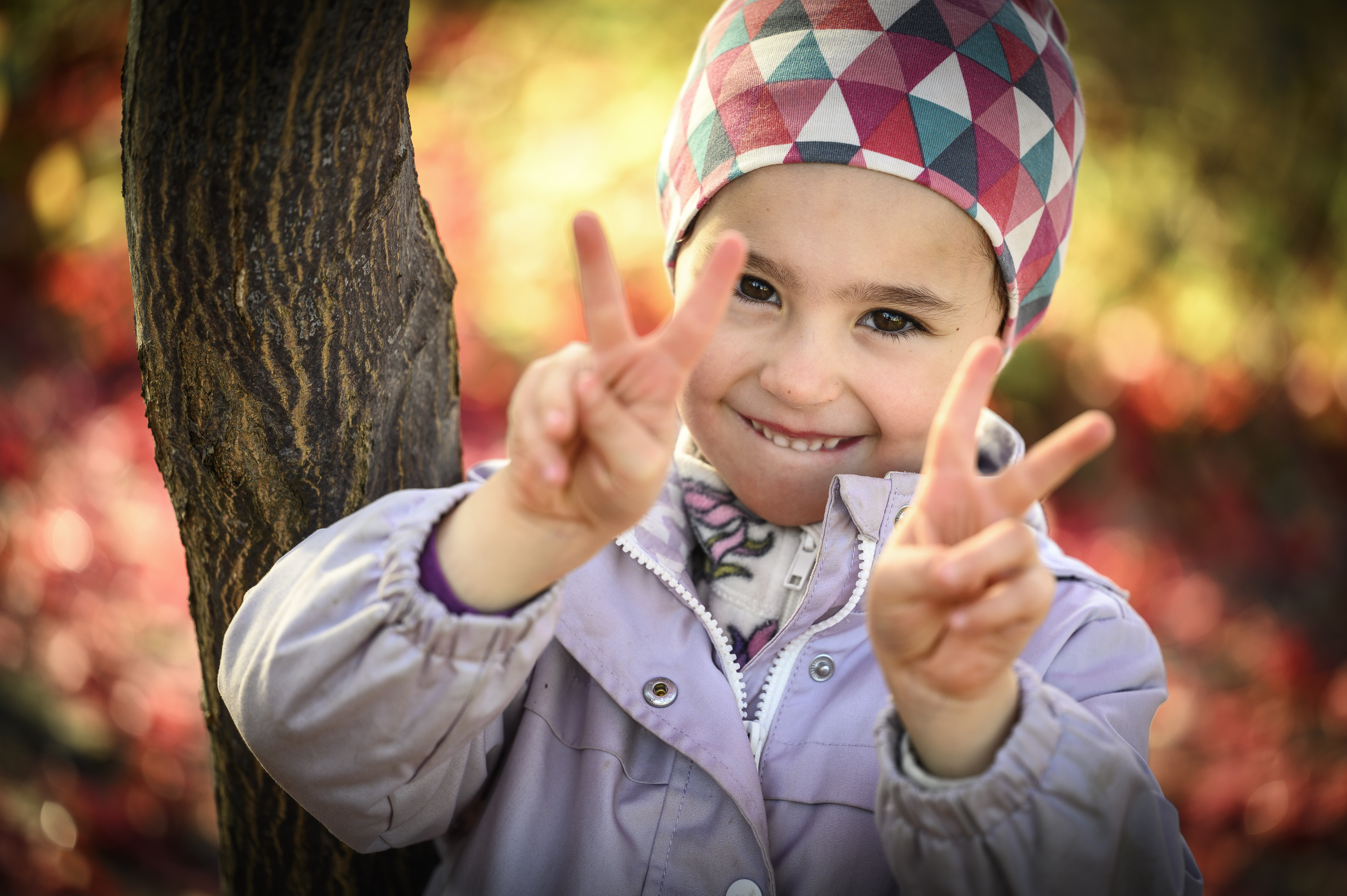 Ett glatt barn med rutig mössa gör V-tecknet med båda händerna mot kameran.