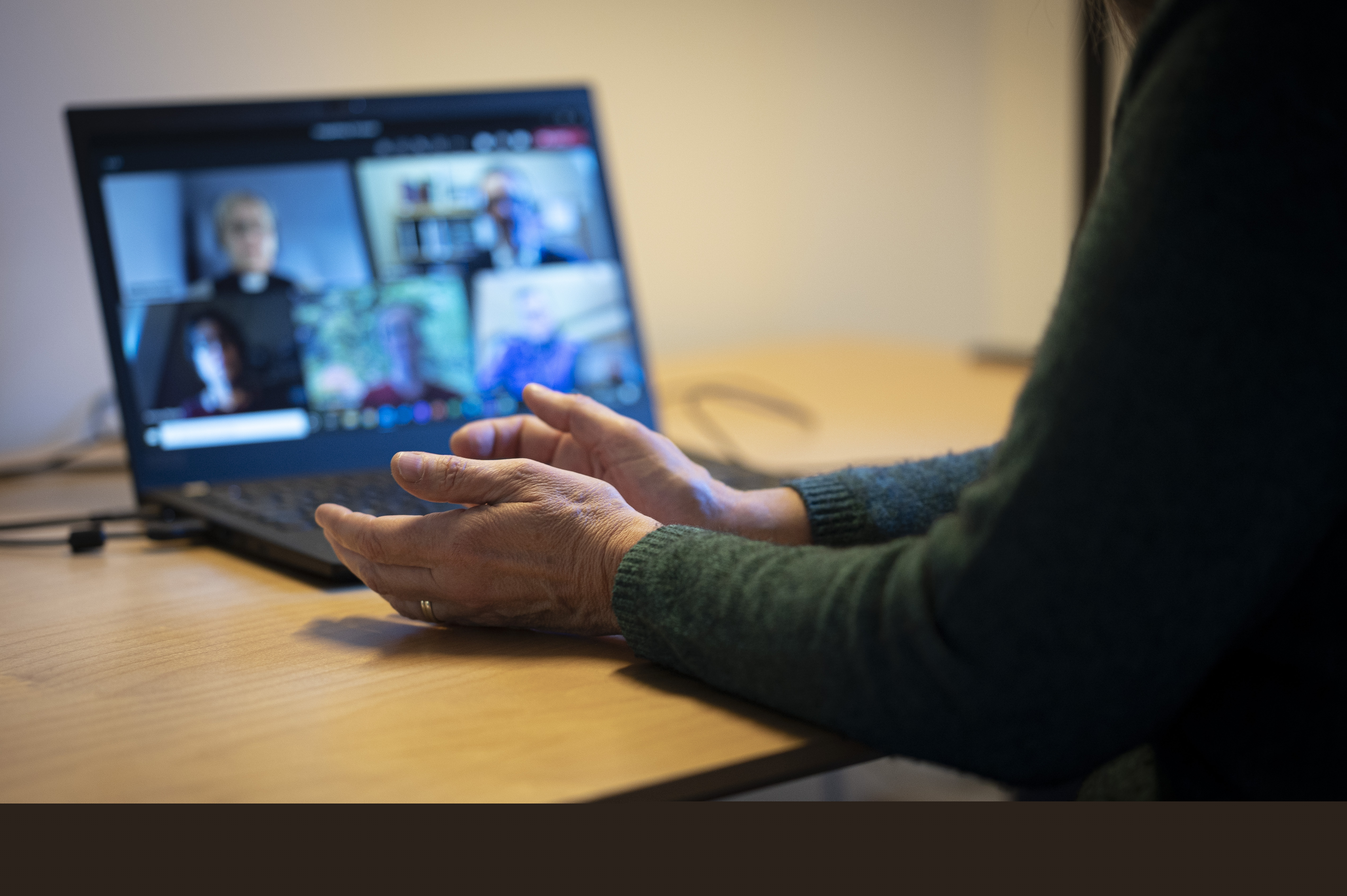 En person sitter vid ett skrivbord och har ett digitalt möte i datorn med några andra.