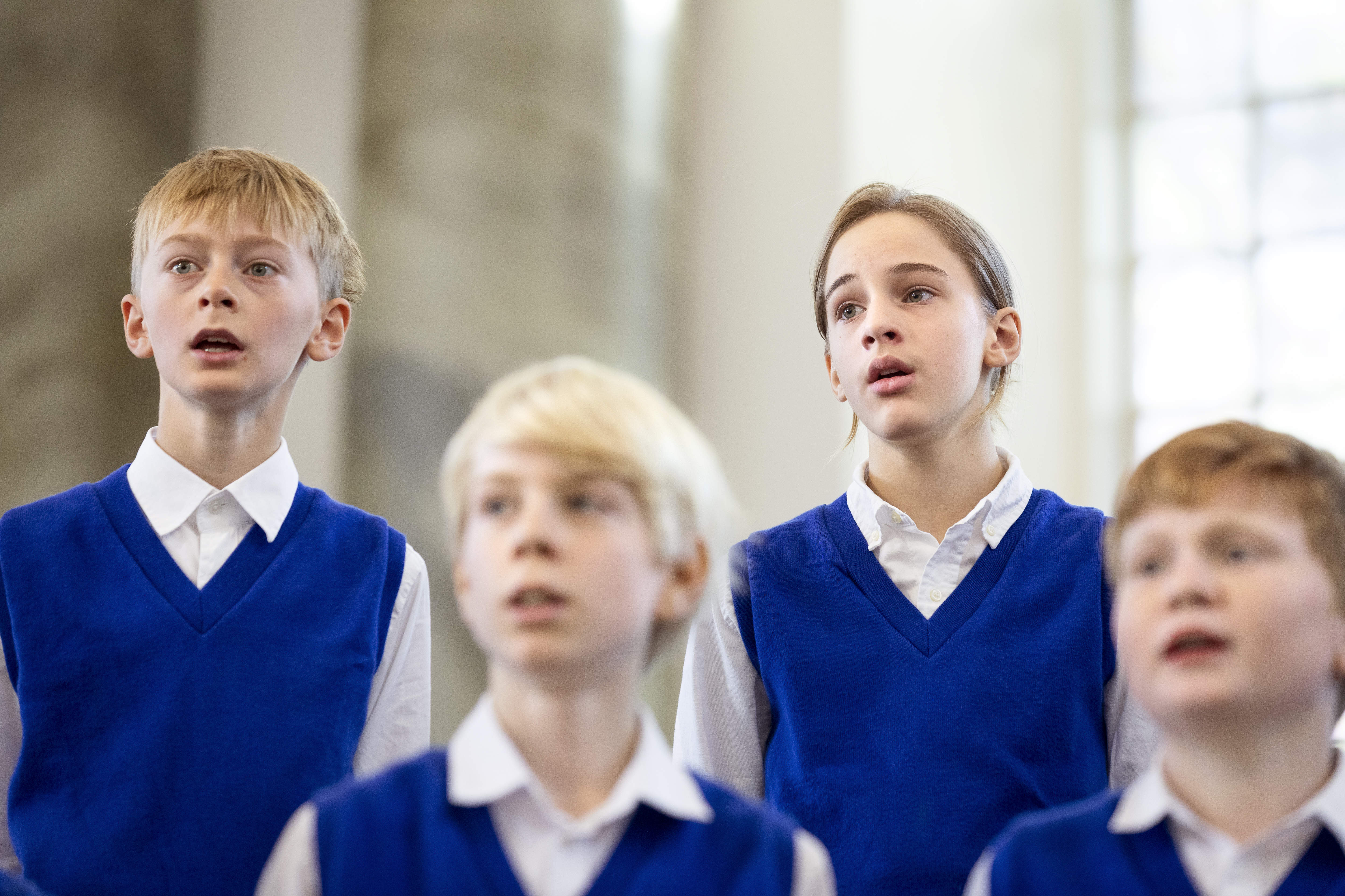 Några medlemmar i en barnkör står och sjunger i blåa slipovrar.