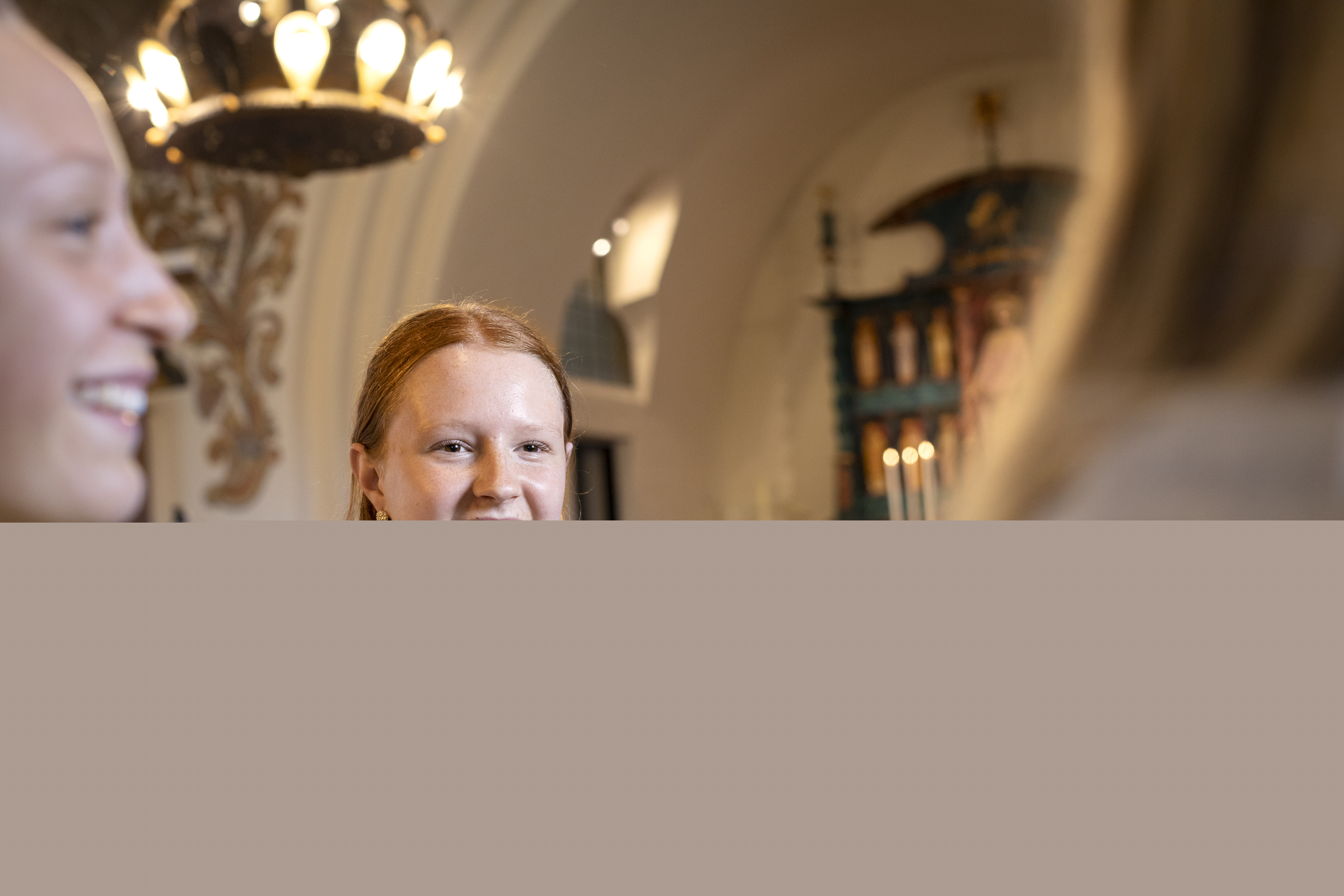 En rödhårig tonårstjej sitter i en kyrkbänk och snackar med några jämnåriga.