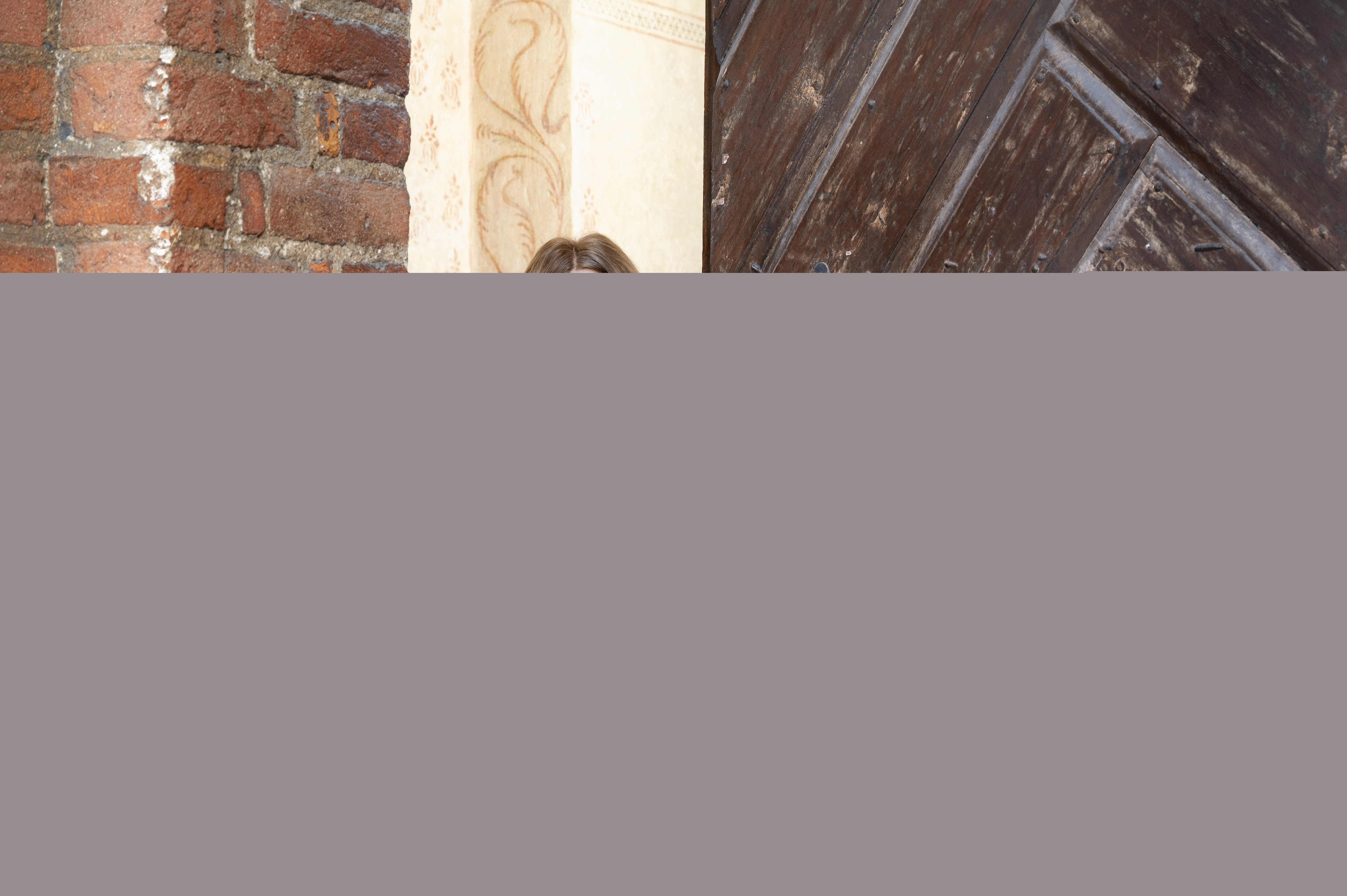 En kvinnlig präst står i dörröppningen till en tegelkyrka.