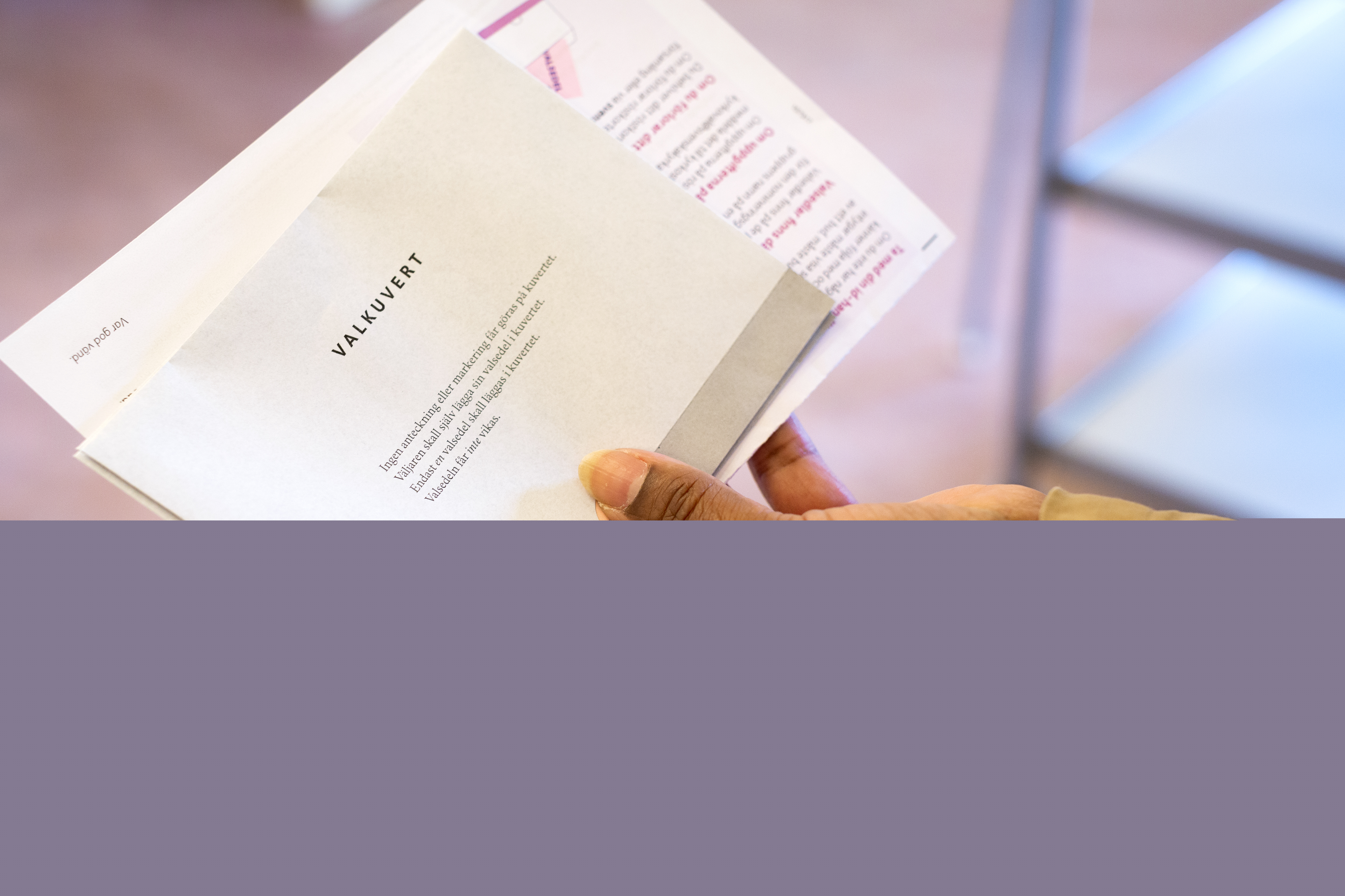 Närbild på en hand som håller ett valkuvert och ett röstkort.