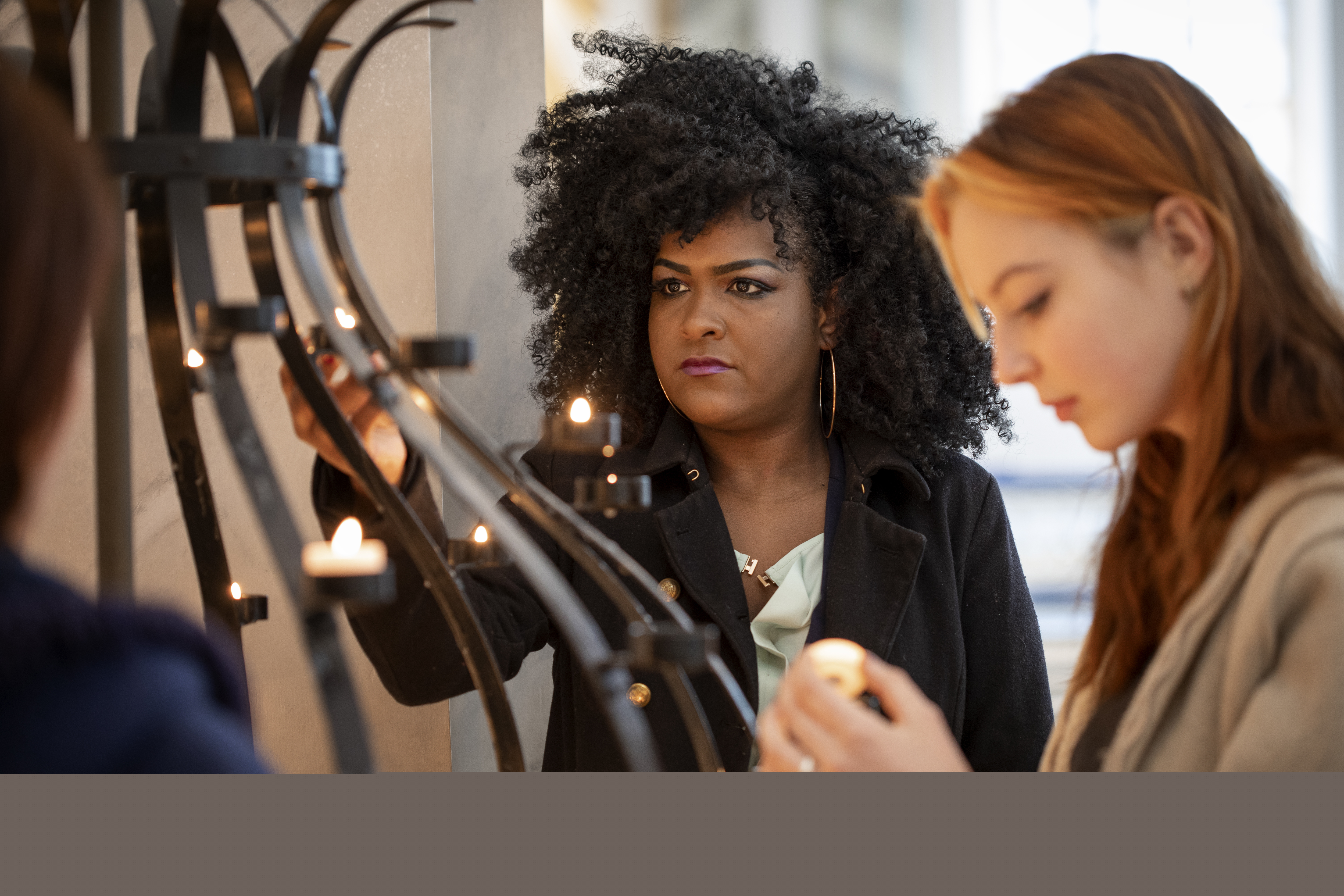 Två unga kvinnor tänder ljus i en ljusbärare.