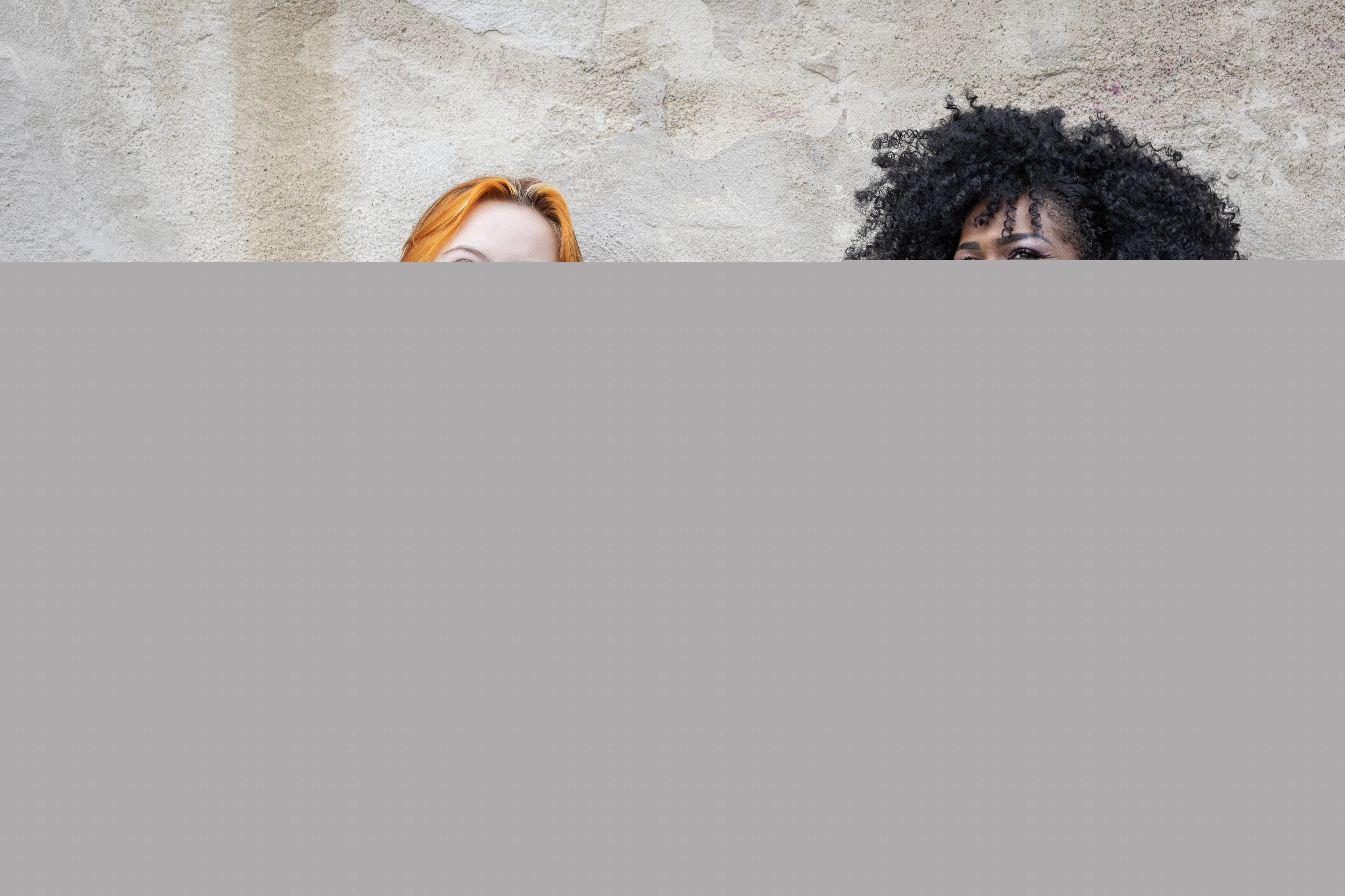 Två unga kvinnor sitter vid en putsad vägg.