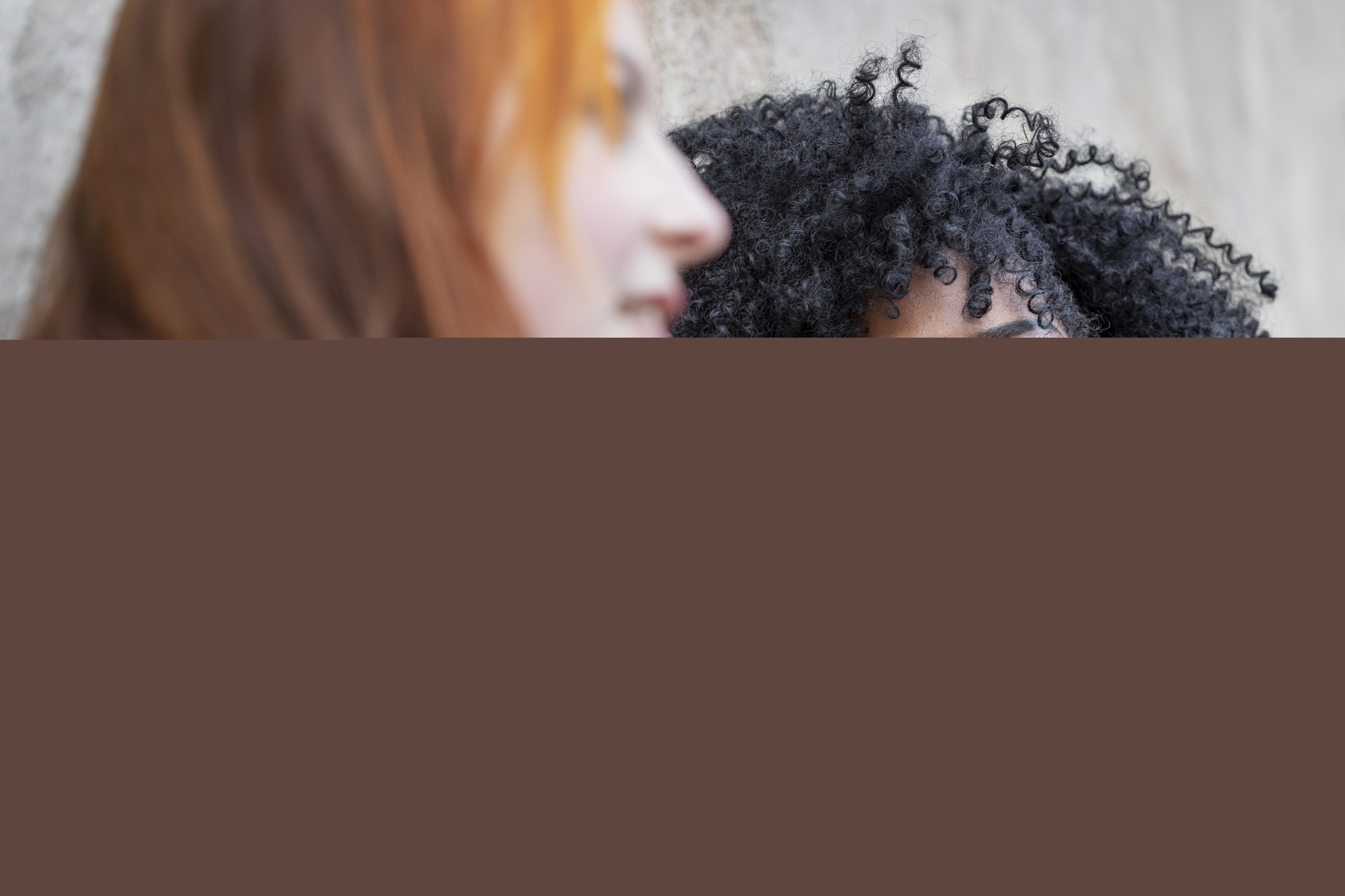 Två unga kvinnor sitter vid en putsad vägg.