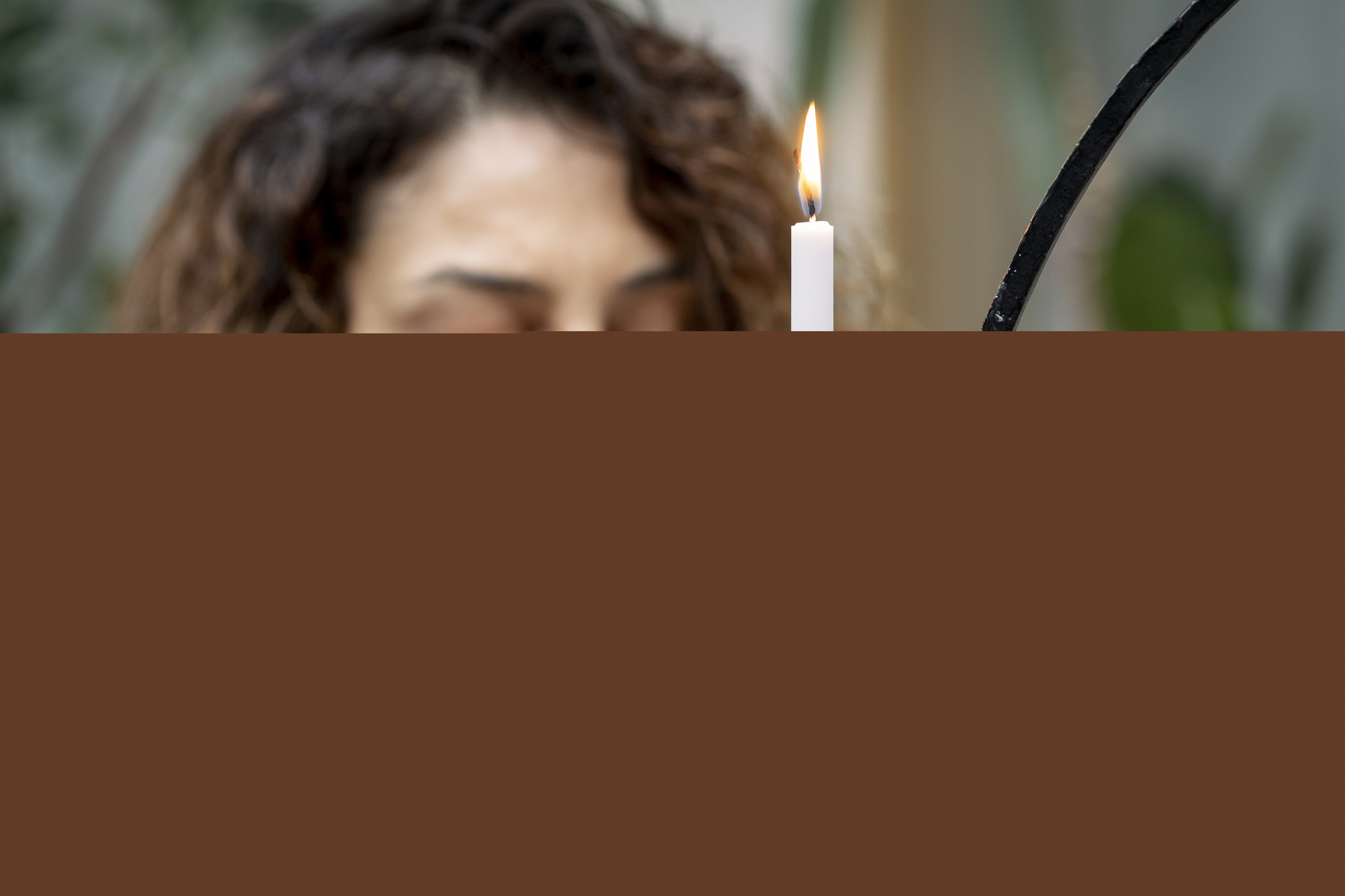 En kvinna med knäppta händer vid en ljusstake.