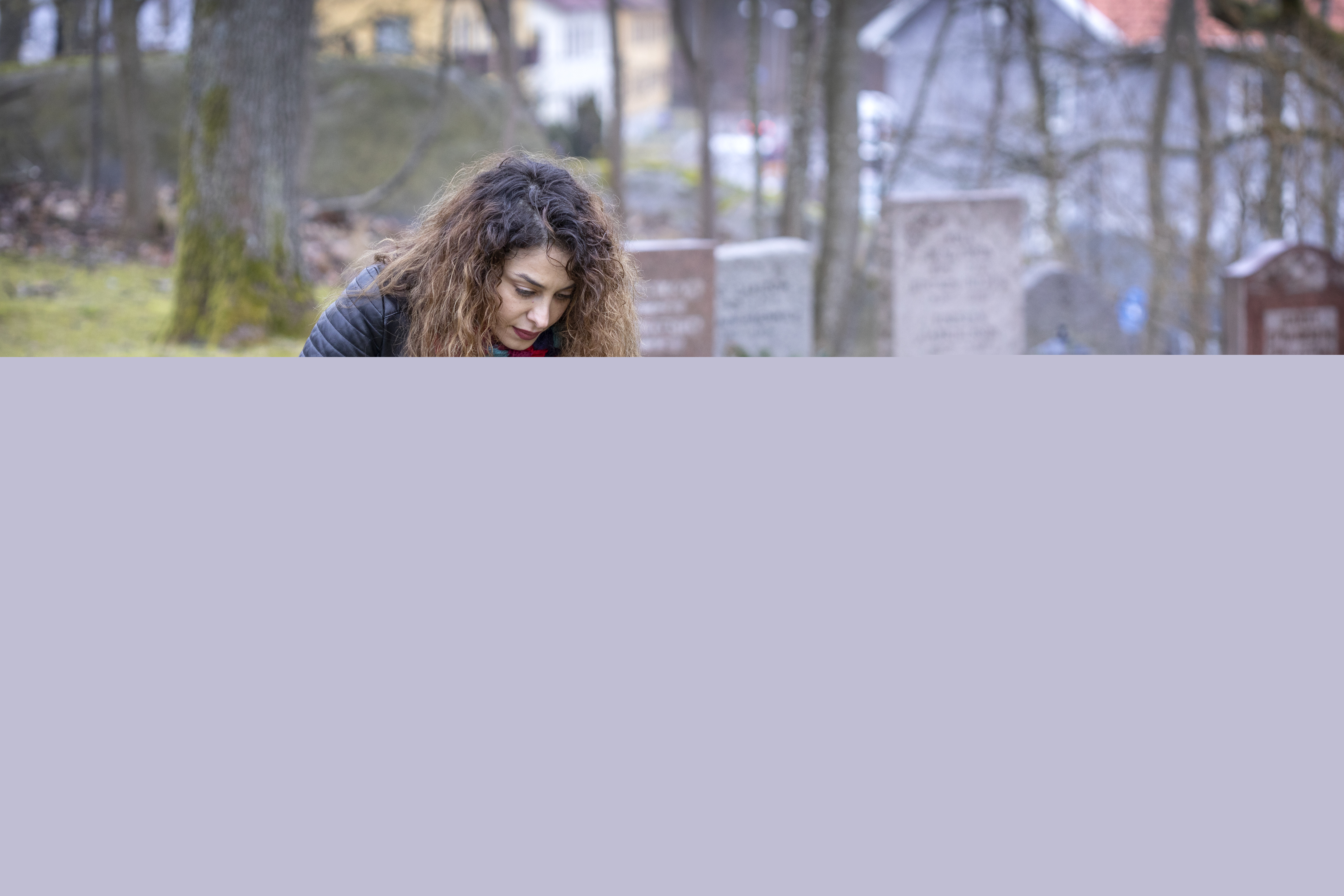 En kvinna på en kyrkogård sitter på huk vid en minnessten.