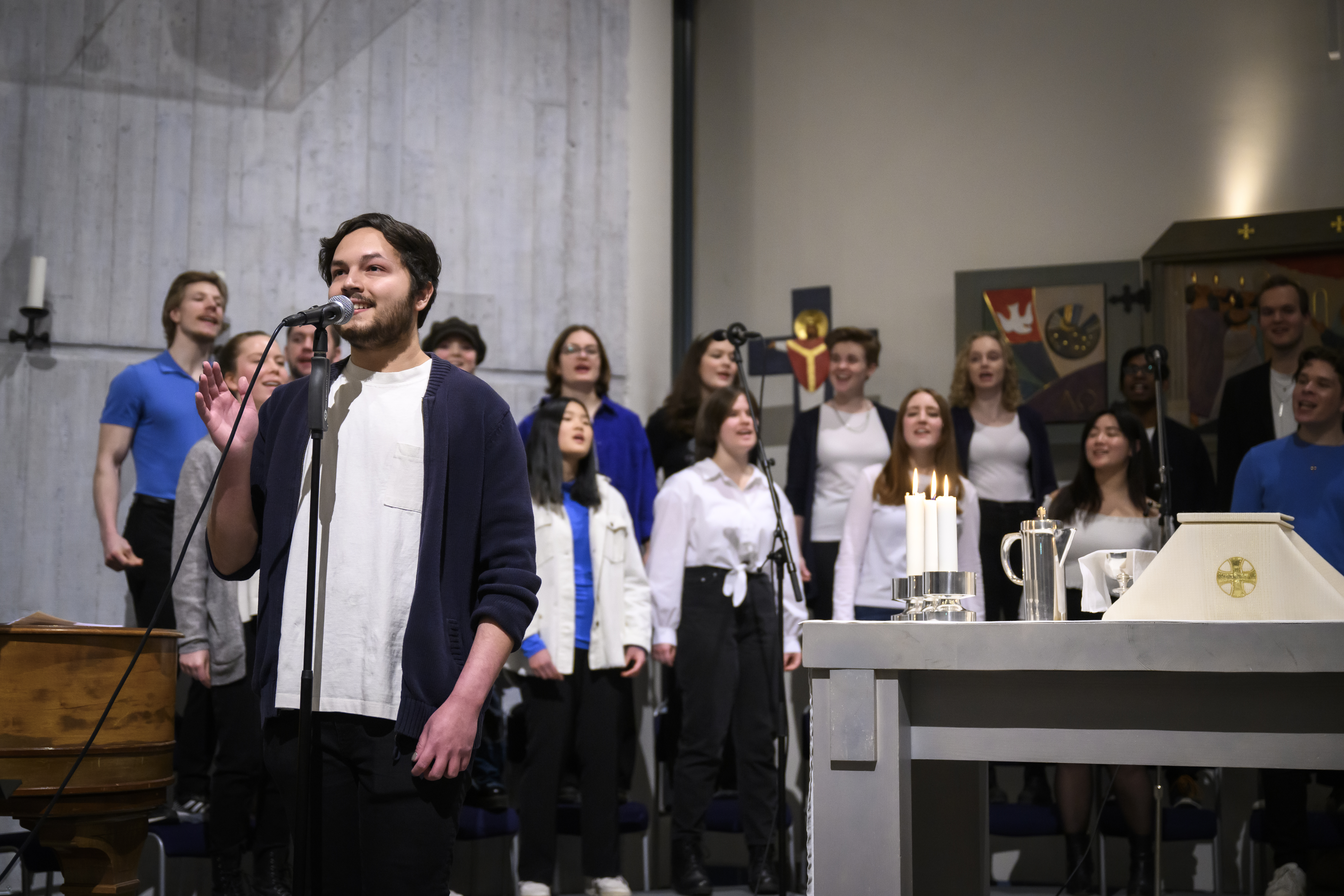 En solist sjunger i en mikrofon, framför en blandad ungdomskör.
