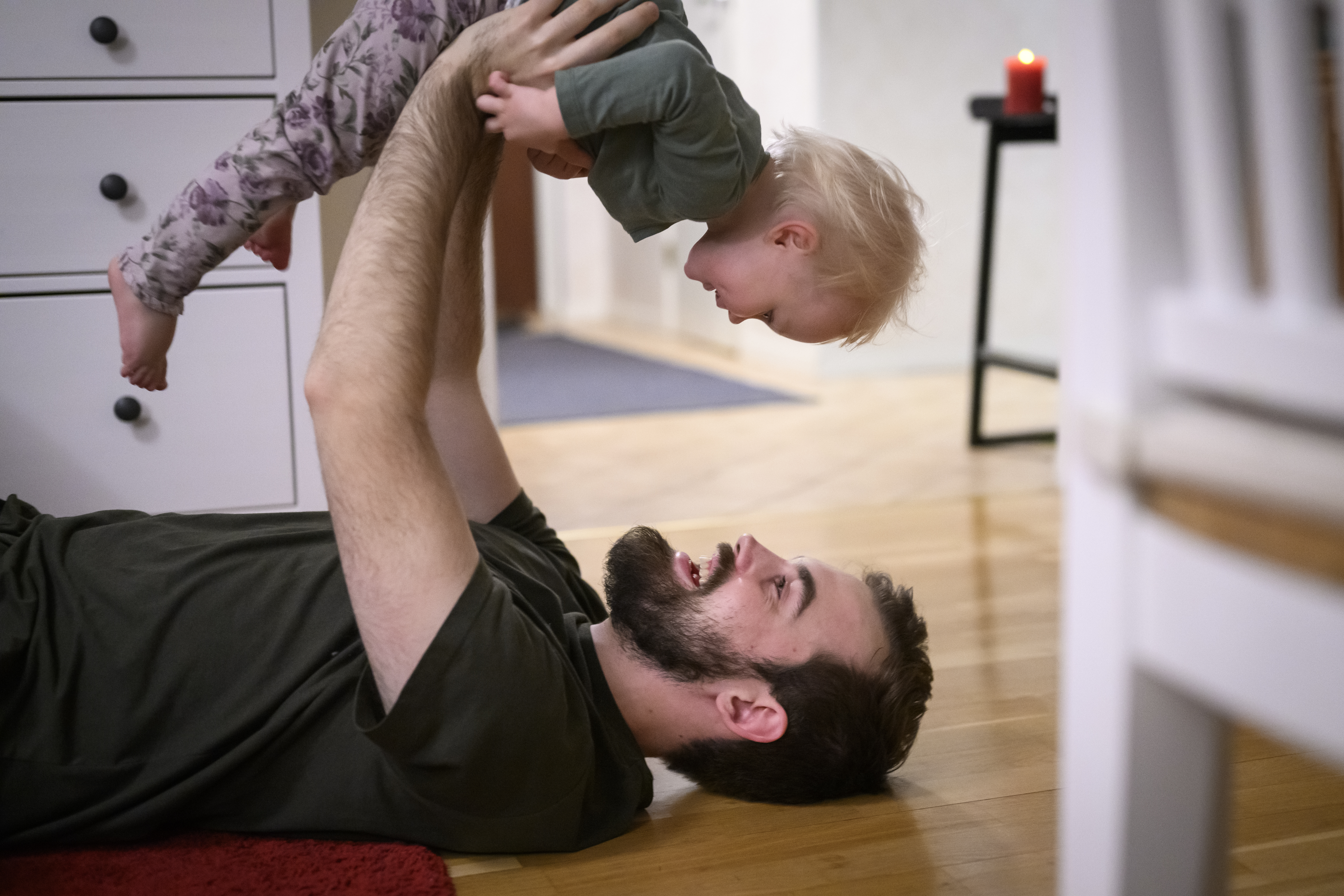 En pappa ligger på golvet och lyfter upp sitt lilla barn på sina armar.
