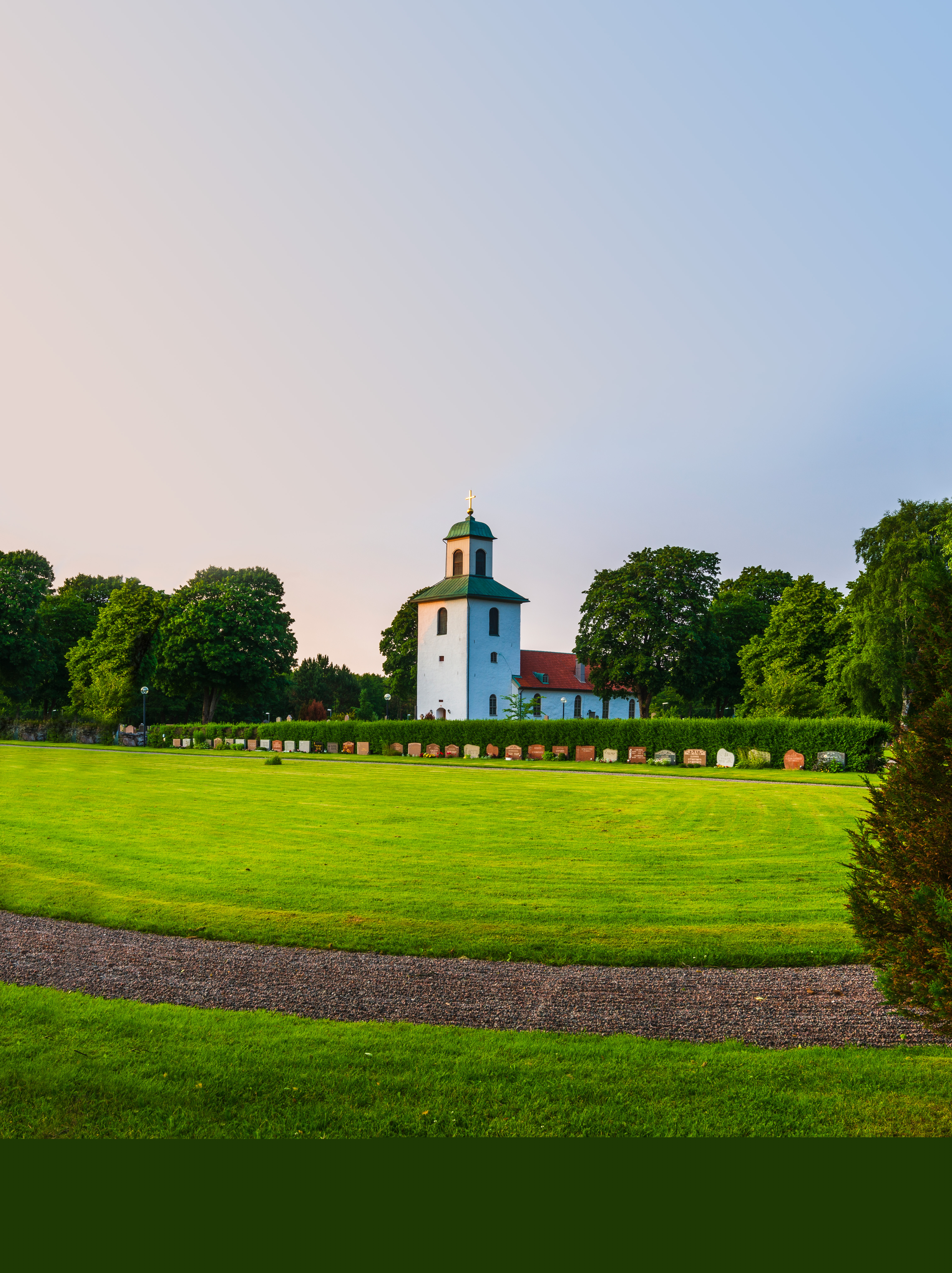 En vit landsbygdskyrka bland lummiga träd.