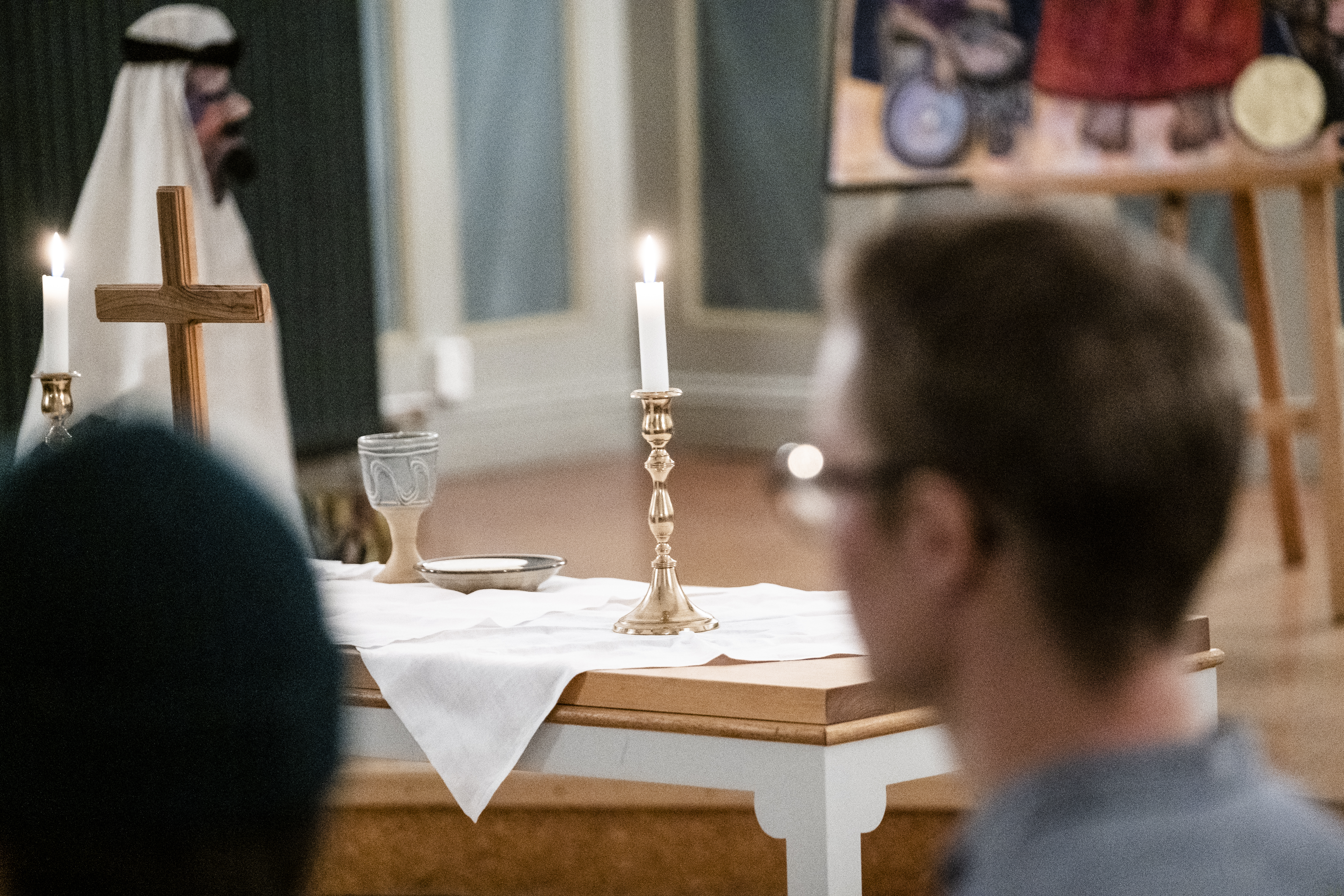 Ett litet träkors och två ljusstakar med tända ljus står på ett altare.