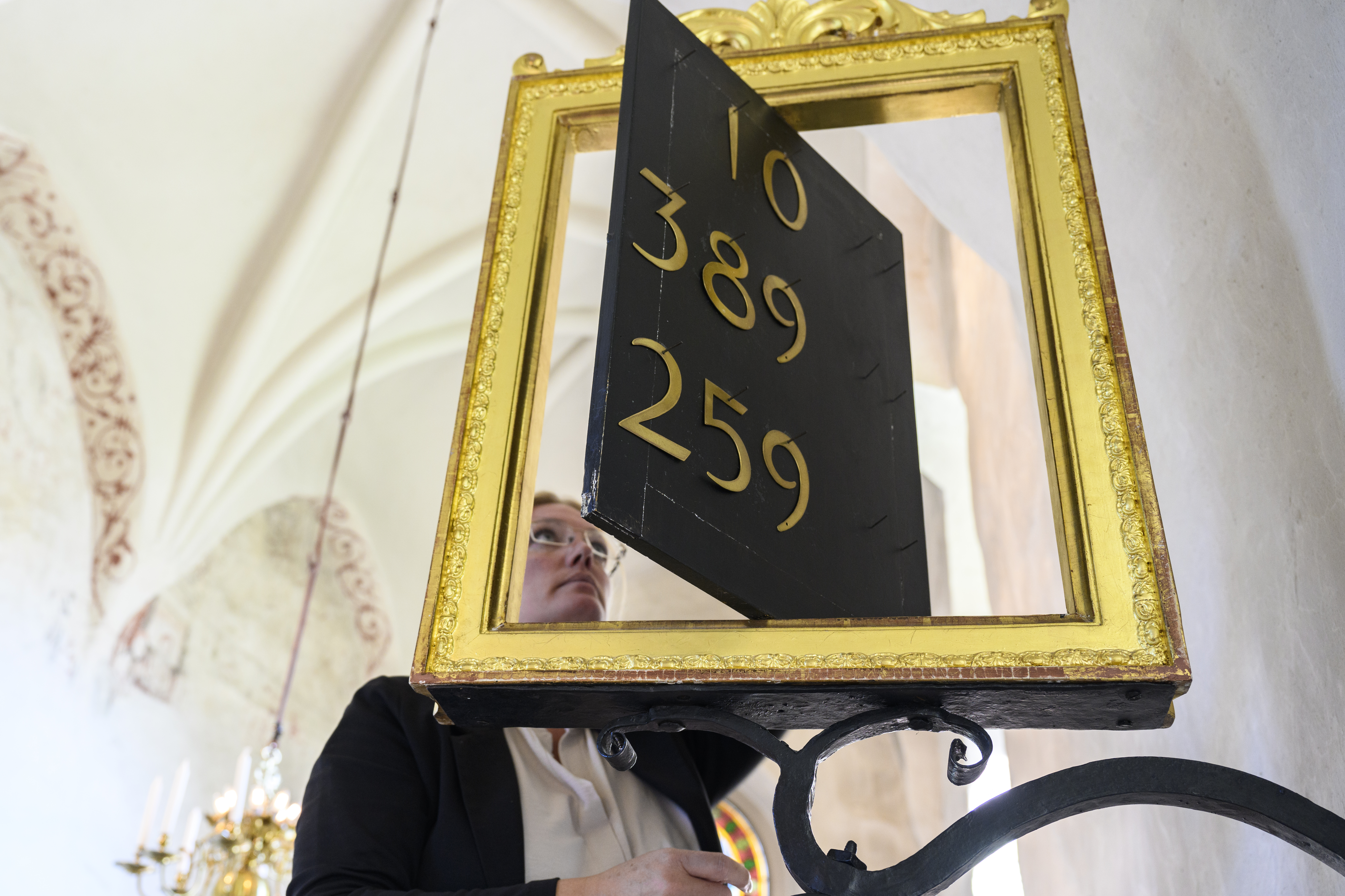 En kvinna justerar siffrorna på en psalmtavla i en kyrka.