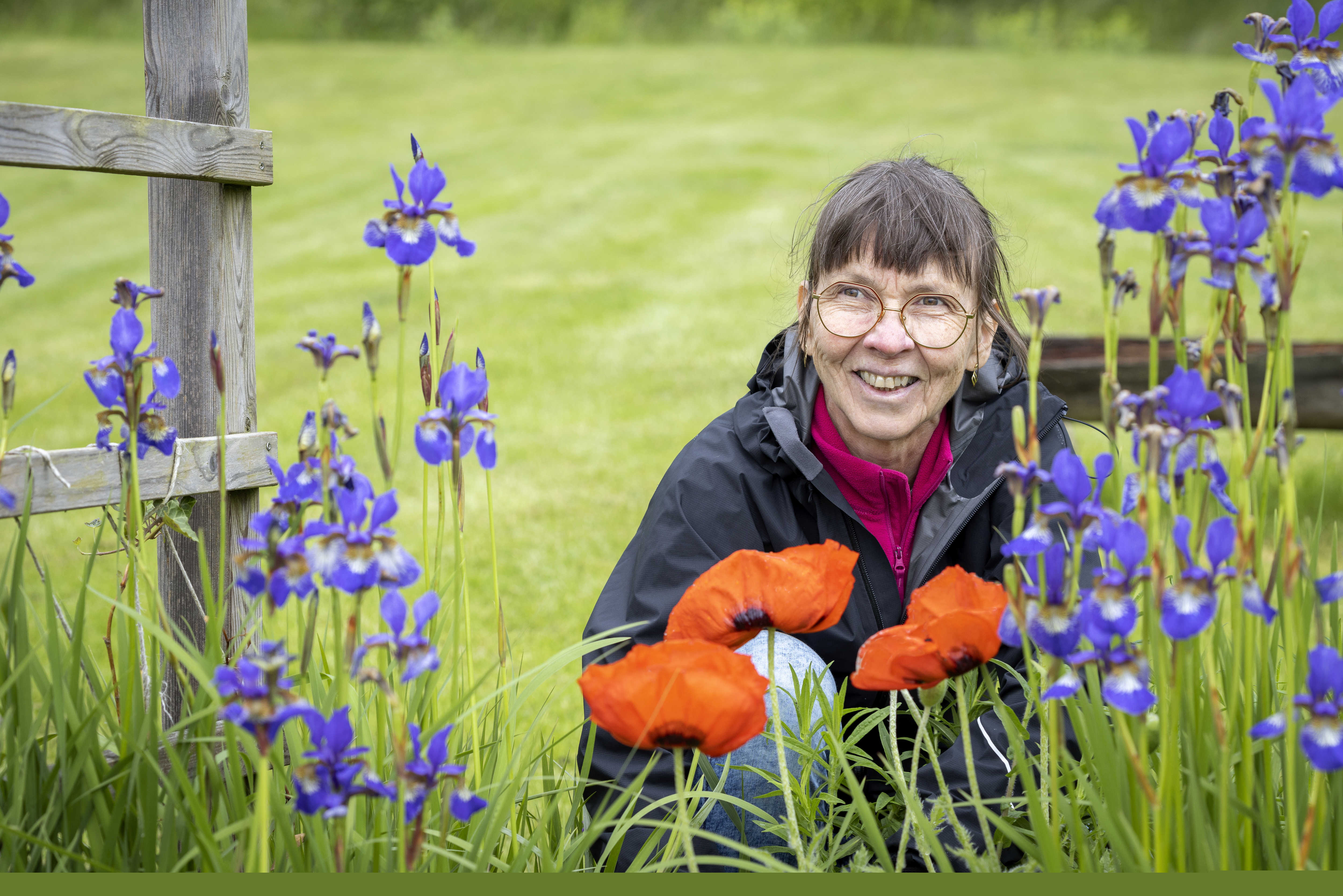 En kvinna sitter på huk vid en blomsteräng och ler.