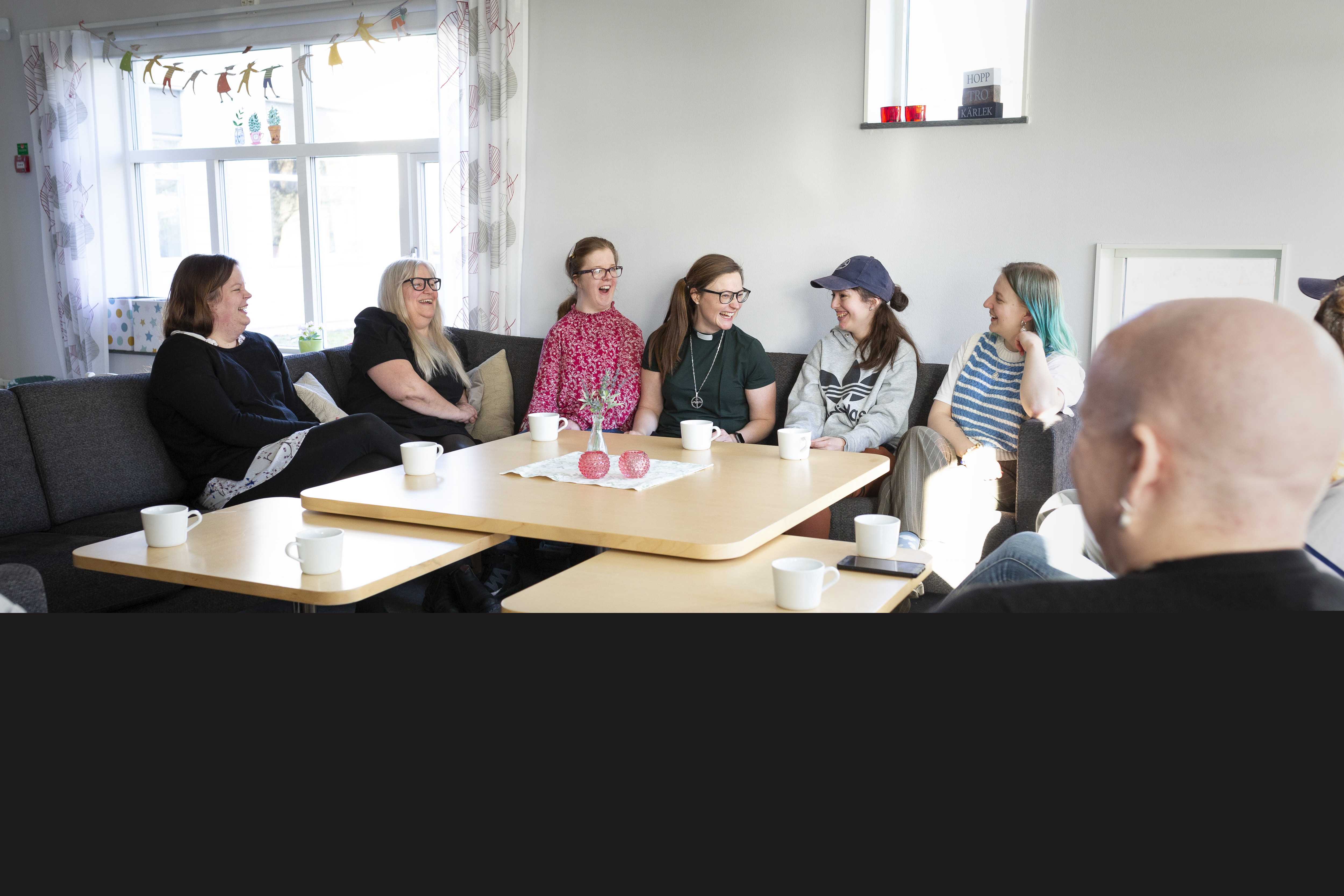 Ett gäng kvinnor i olika åldrar och en kvinnlig diakon sitter i en soffa och skrattar tillsammans.