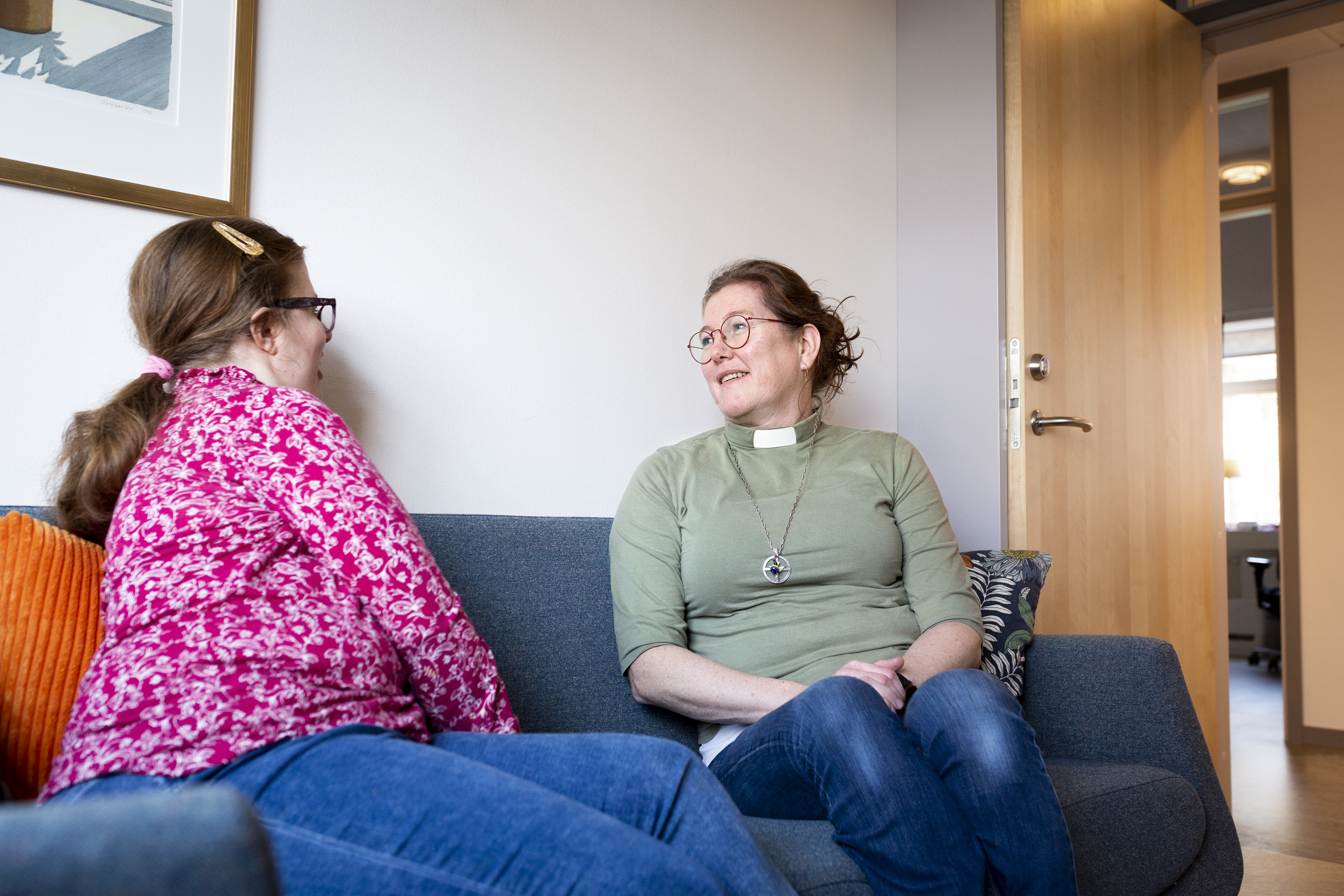 En kvinnlig diakon sitter och samtalar med en ung tjej i en soffa.