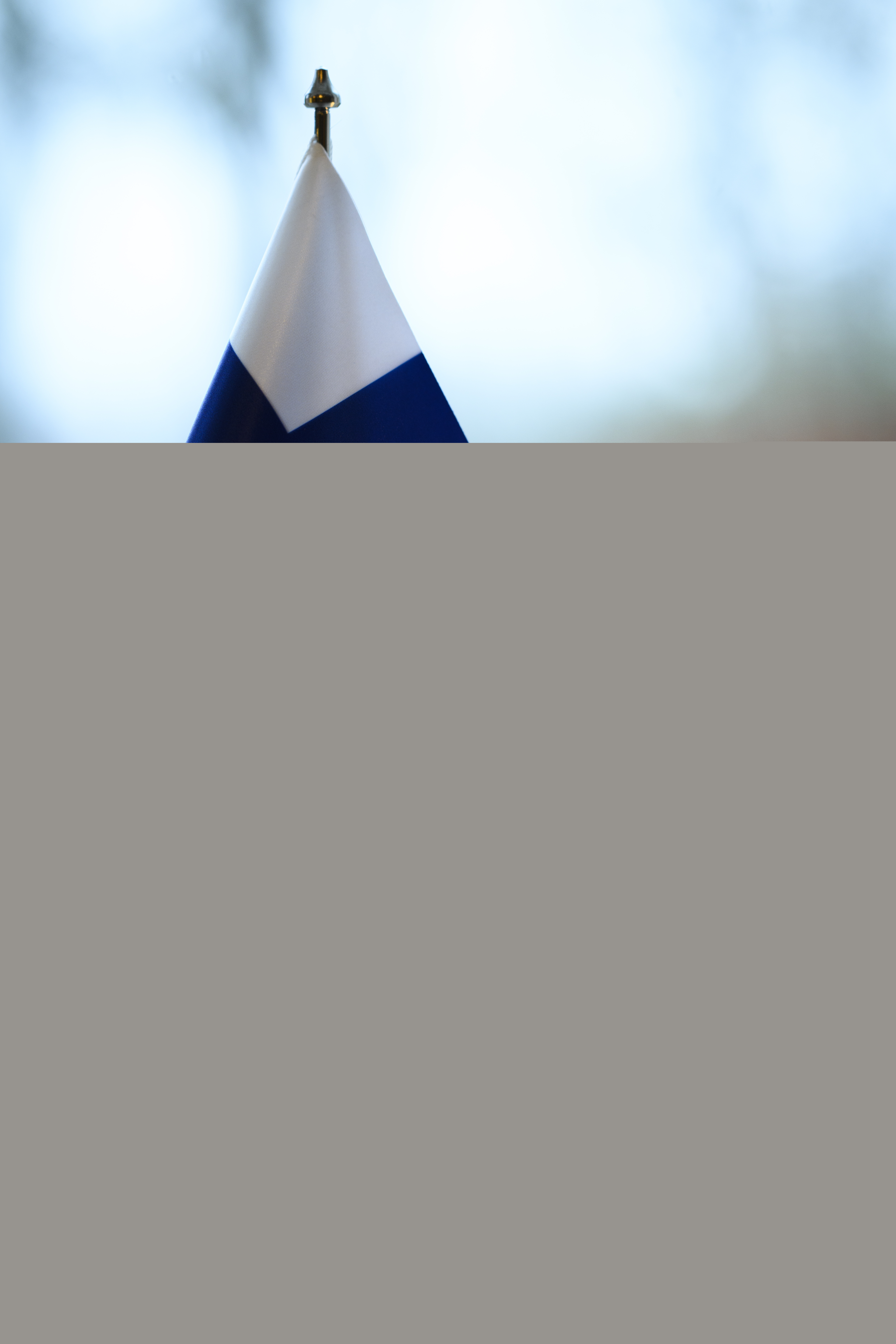 En finsk bordsflagga och ett brinnande stearinljus står i ett fönster.