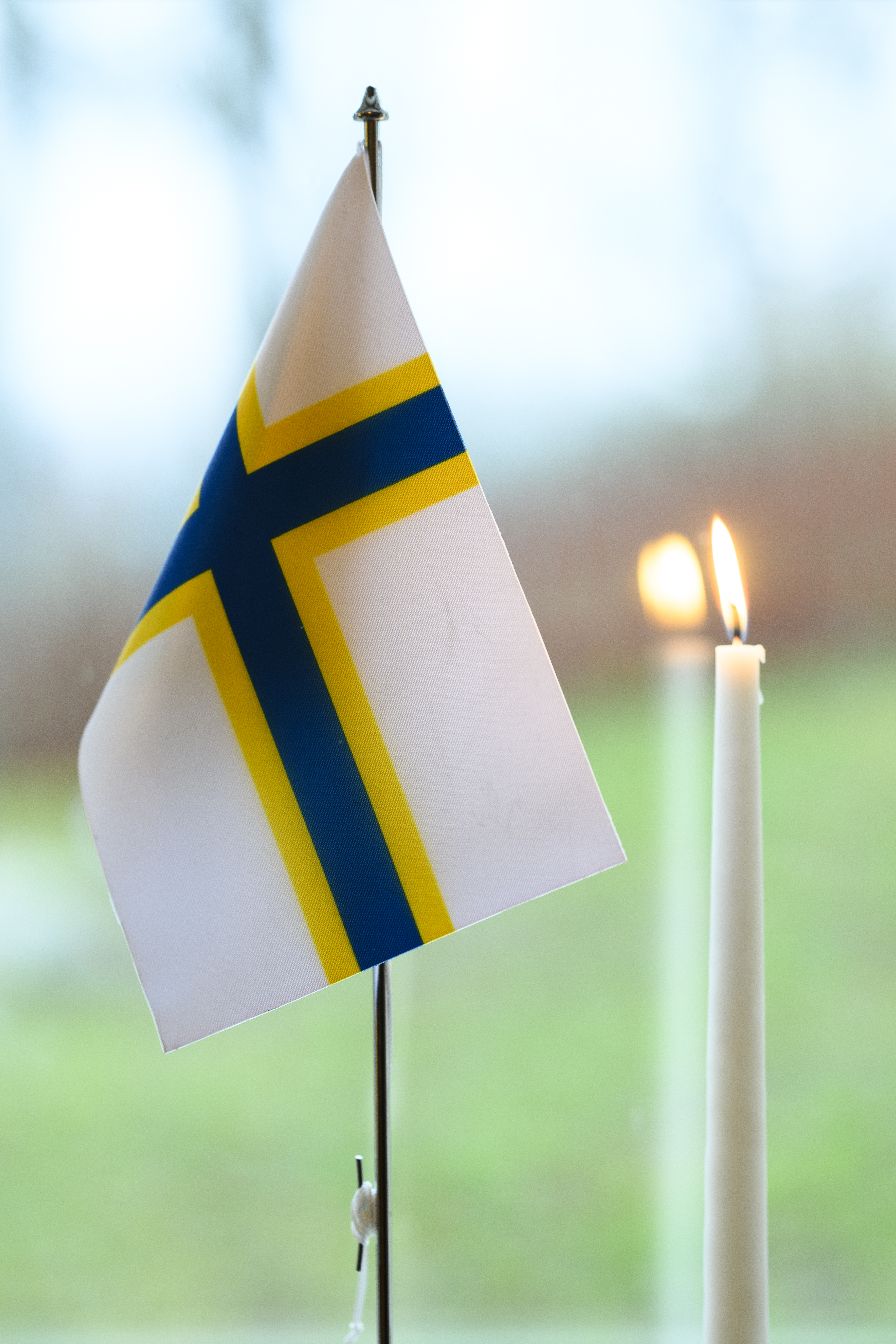 En sverigefinsk bordsflagga och ett brinnande stearinljus står i ett fönster.