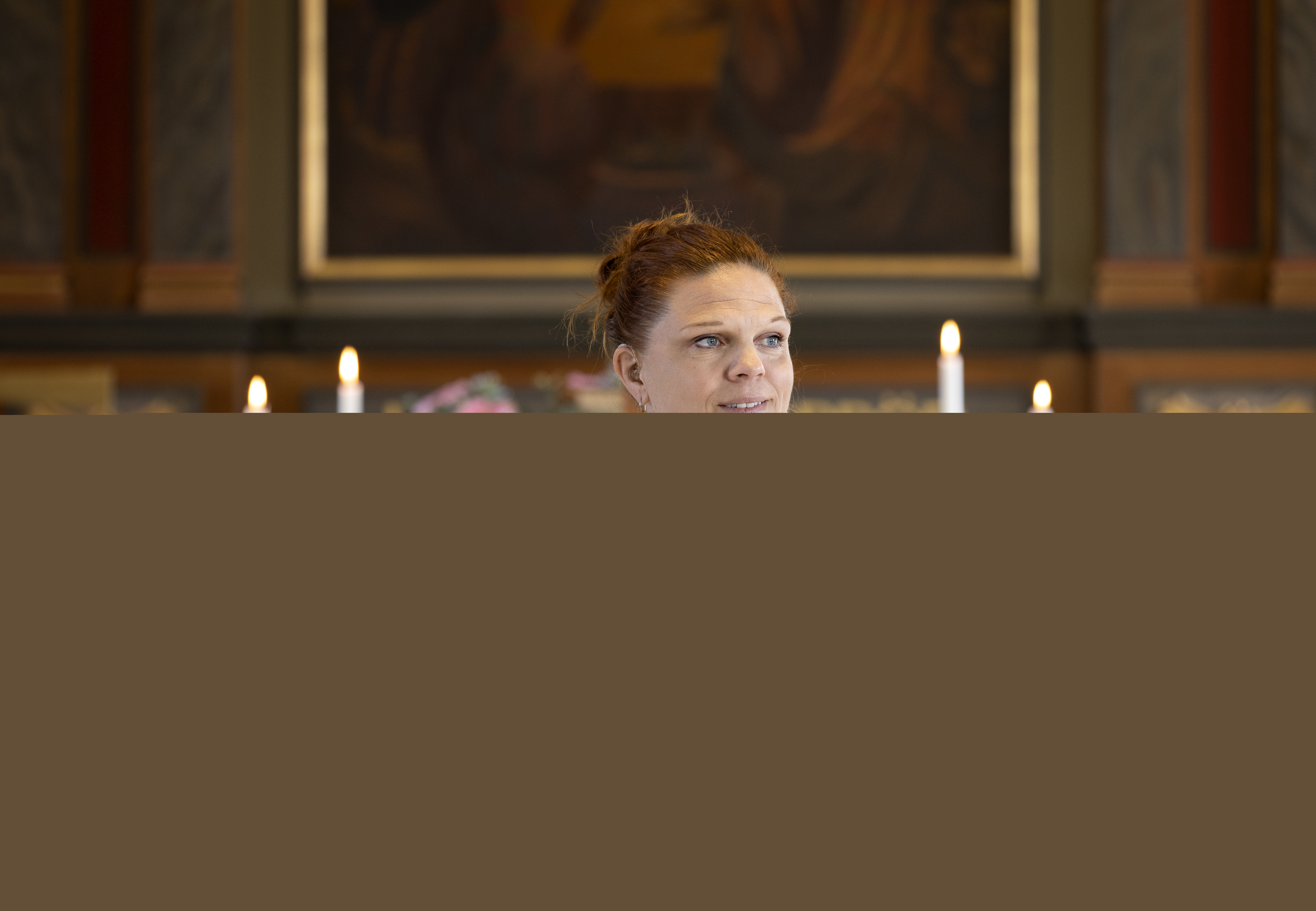 En kvinnlig präst i vit kåpa står vid koret och håller båda händerna mot hjärtat.