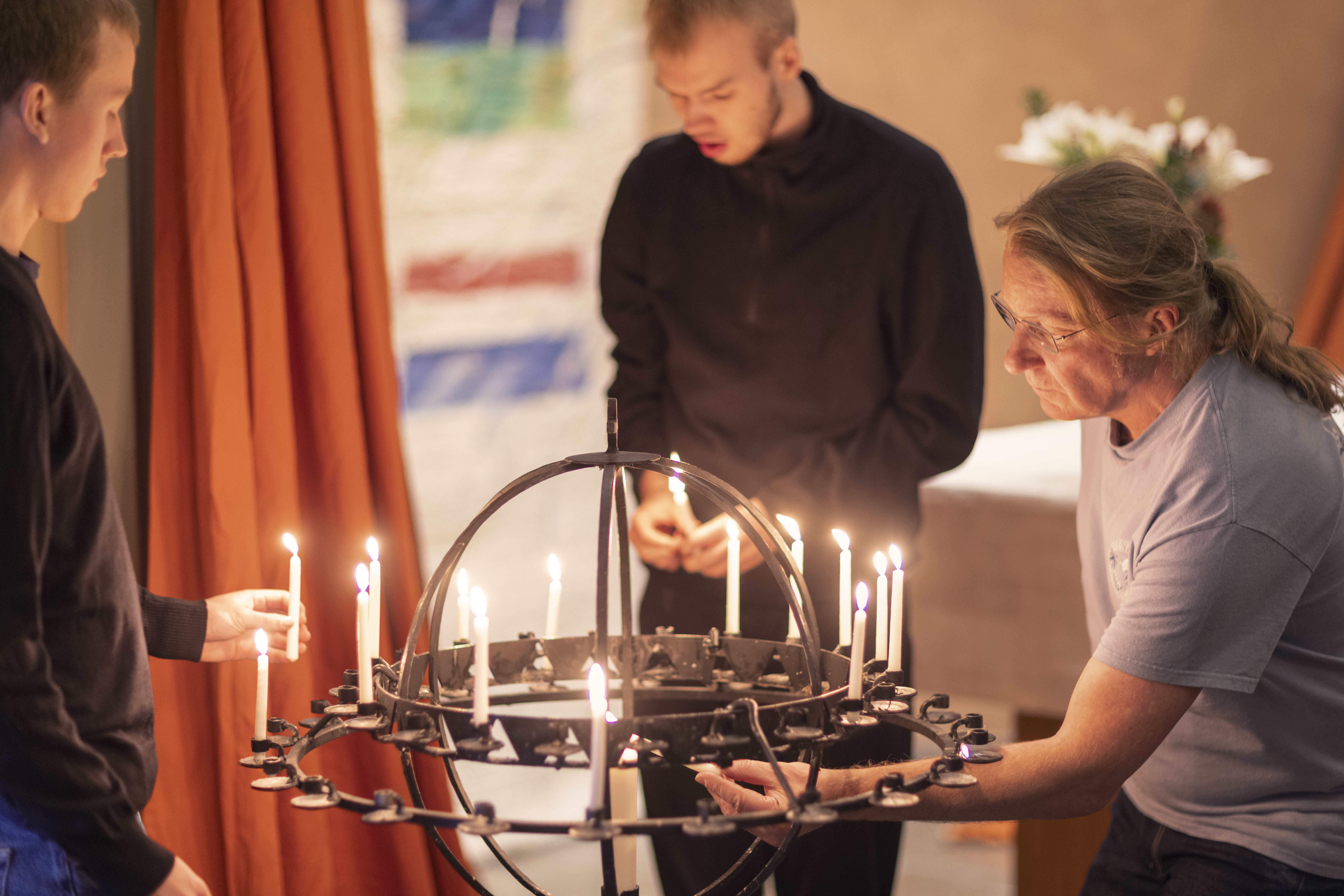 Tre personer sätter ner tända ljus i en ljusbärare.