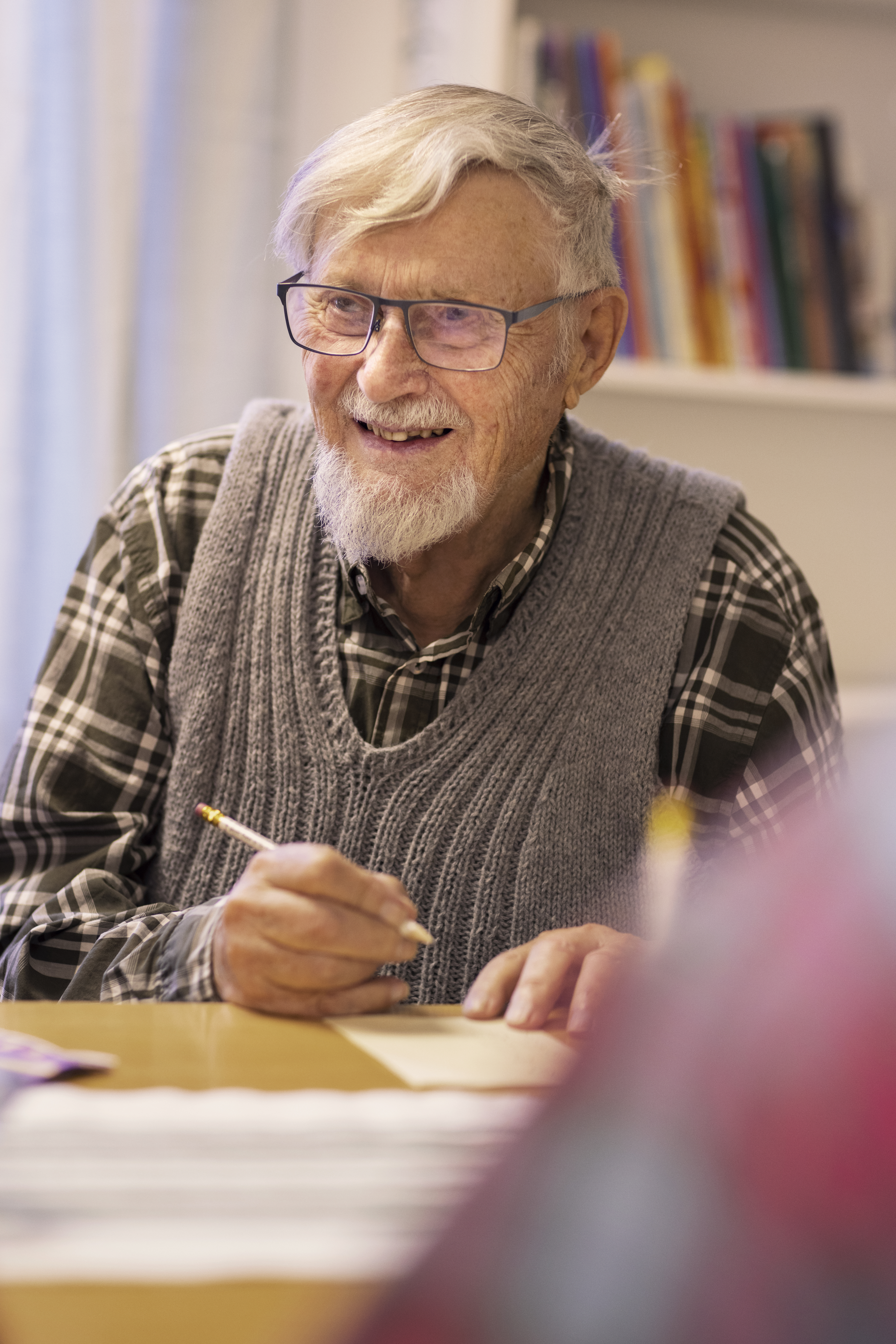 En äldre man sitter vid ett bord och ler stort.